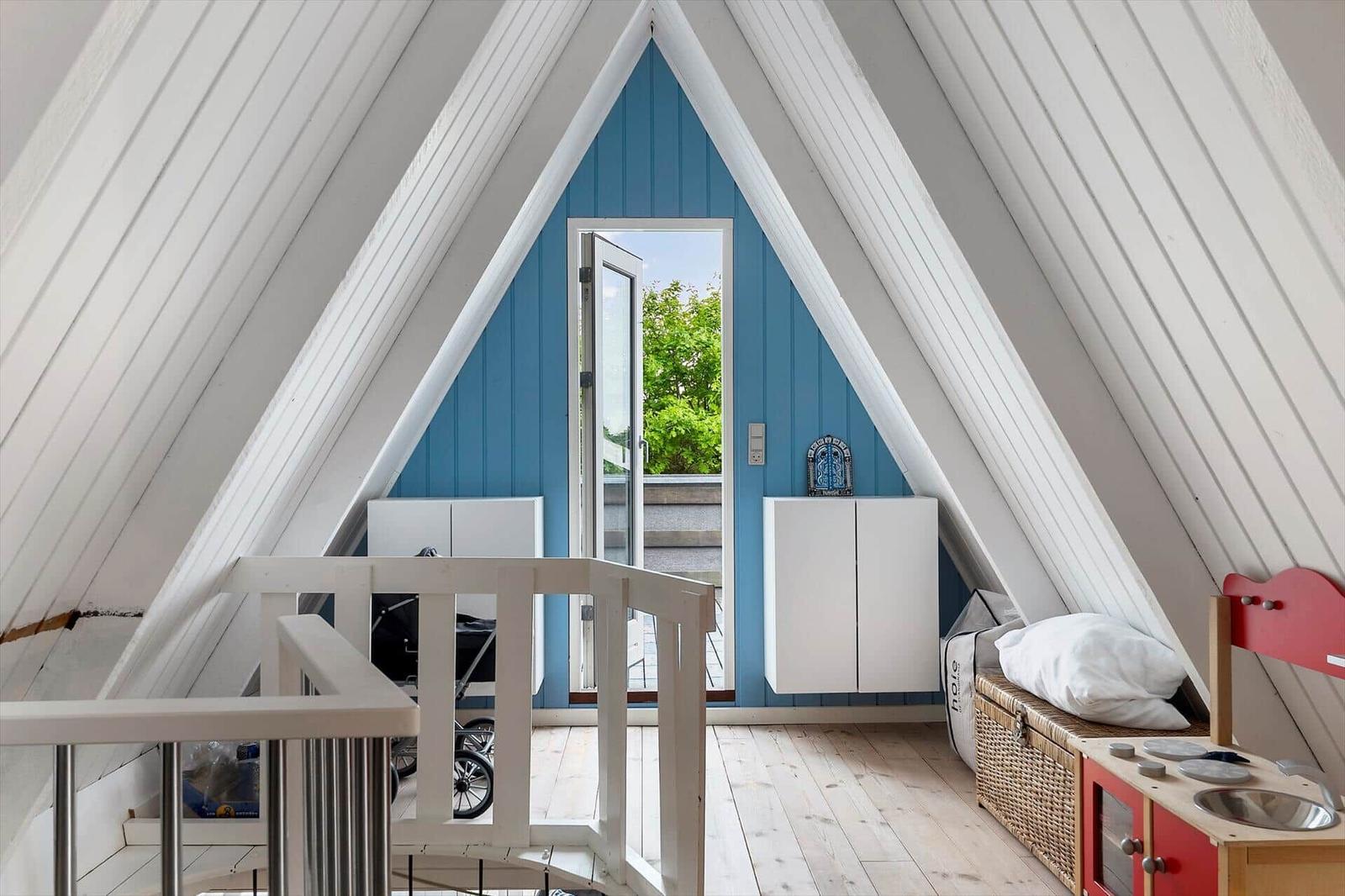 Dachgeschoss mit blauer Wand, weißen Schränken und Spielzeugküche. Tür führt nach draußen.