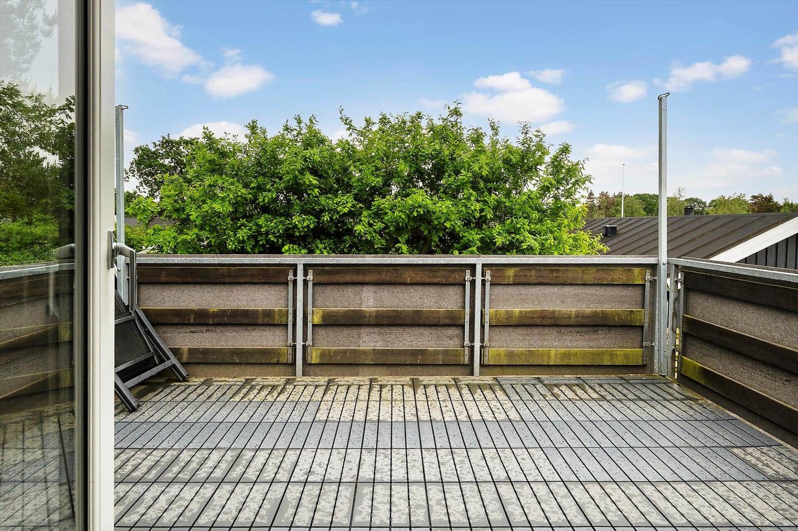 Terrasse mit Holzgeländer und Blick auf grüne Bäume unter blauem Himmel.