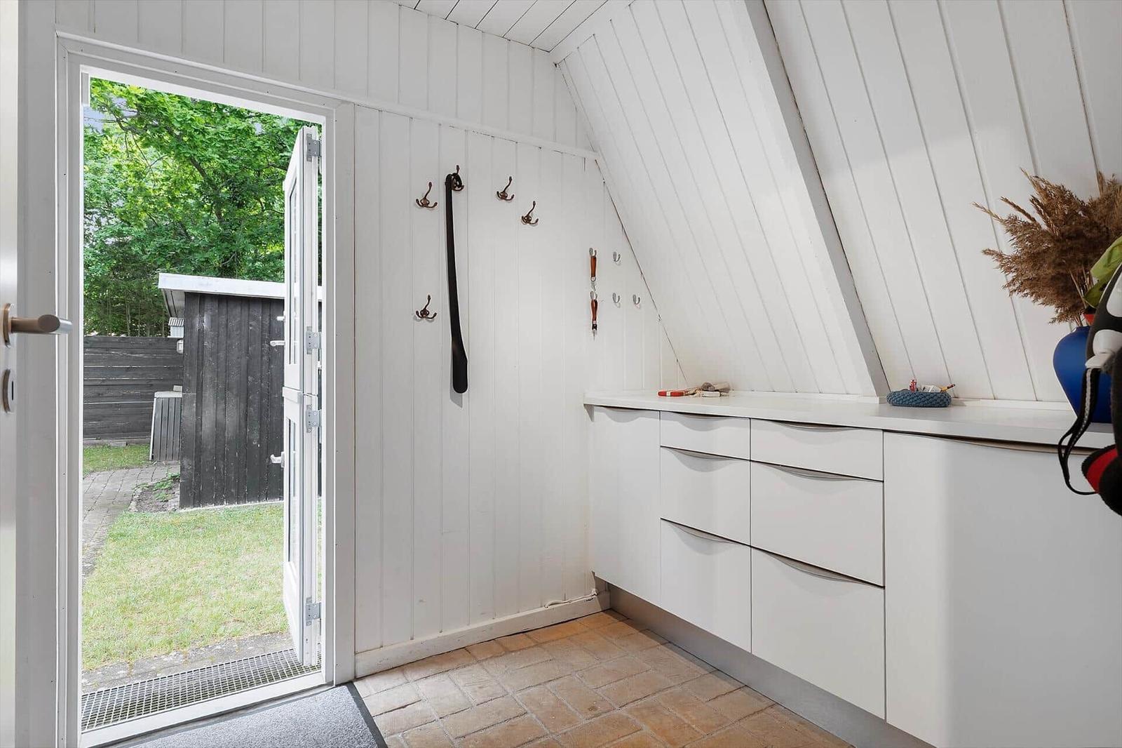Eingangsbereich mit weißen Wänden, Garderobe und Küchenzeile. Tür führt nach draußen.