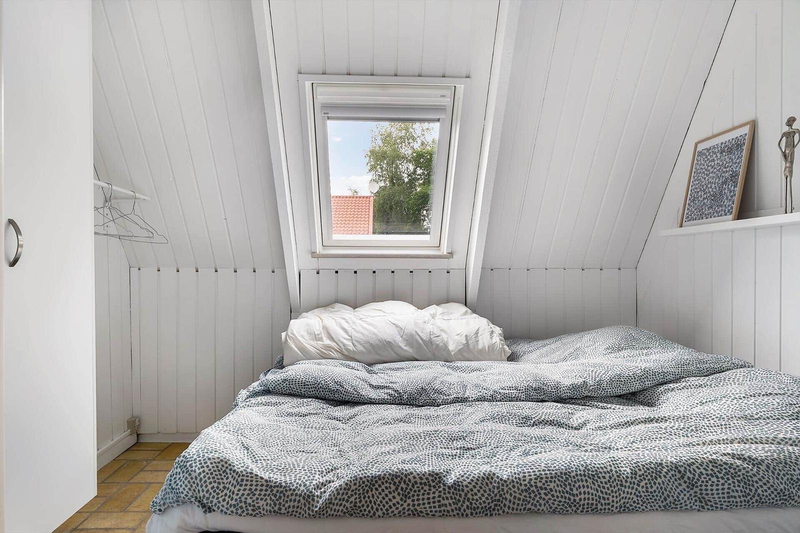 Schlafzimmer mit Dachfenster, weißer Holzwand und Bett mit Musterdecke.