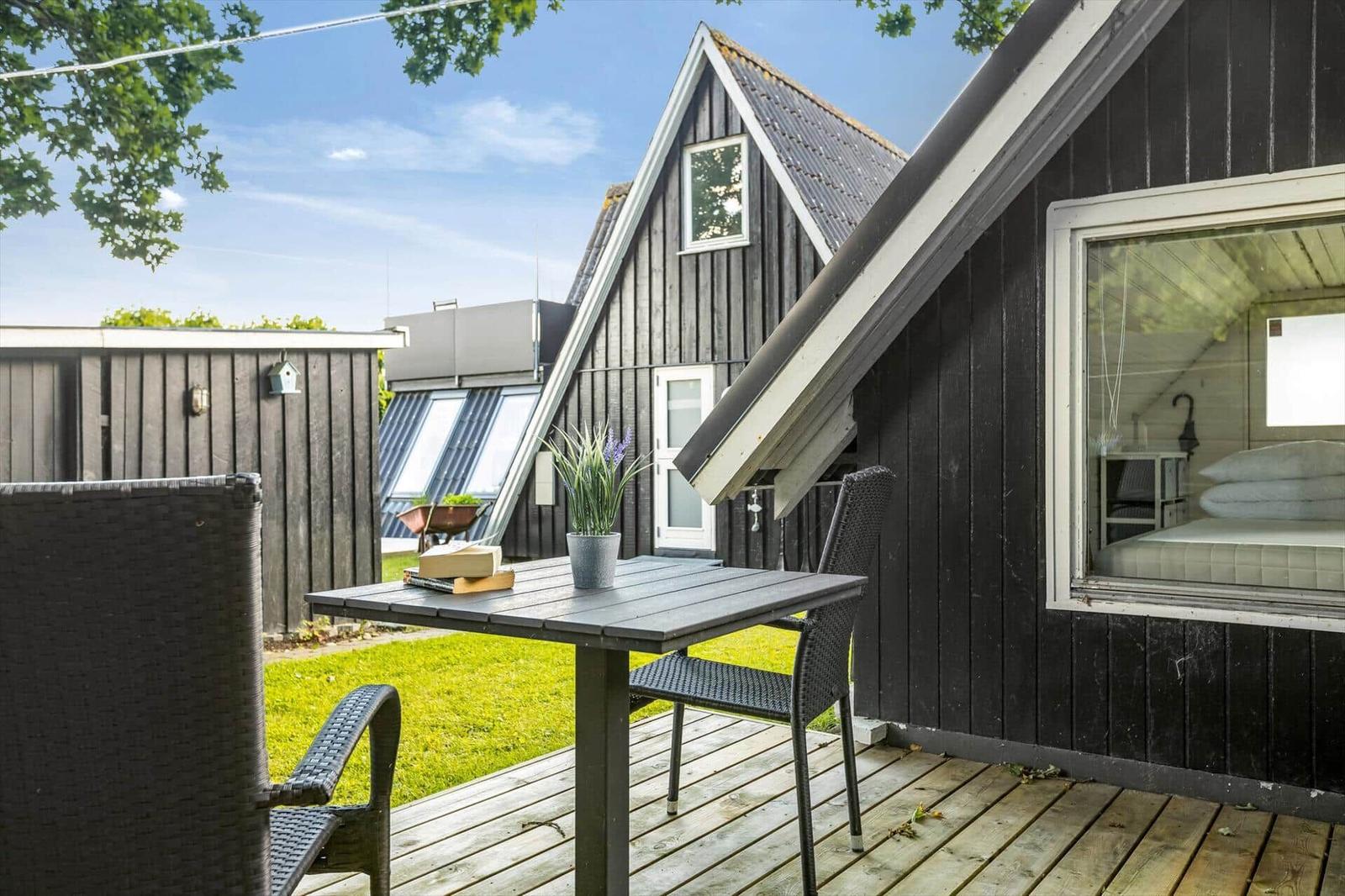 Terrasse mit Tisch und Stühlen vor einem schwarzen Holzhaus mit Blick ins Innere.