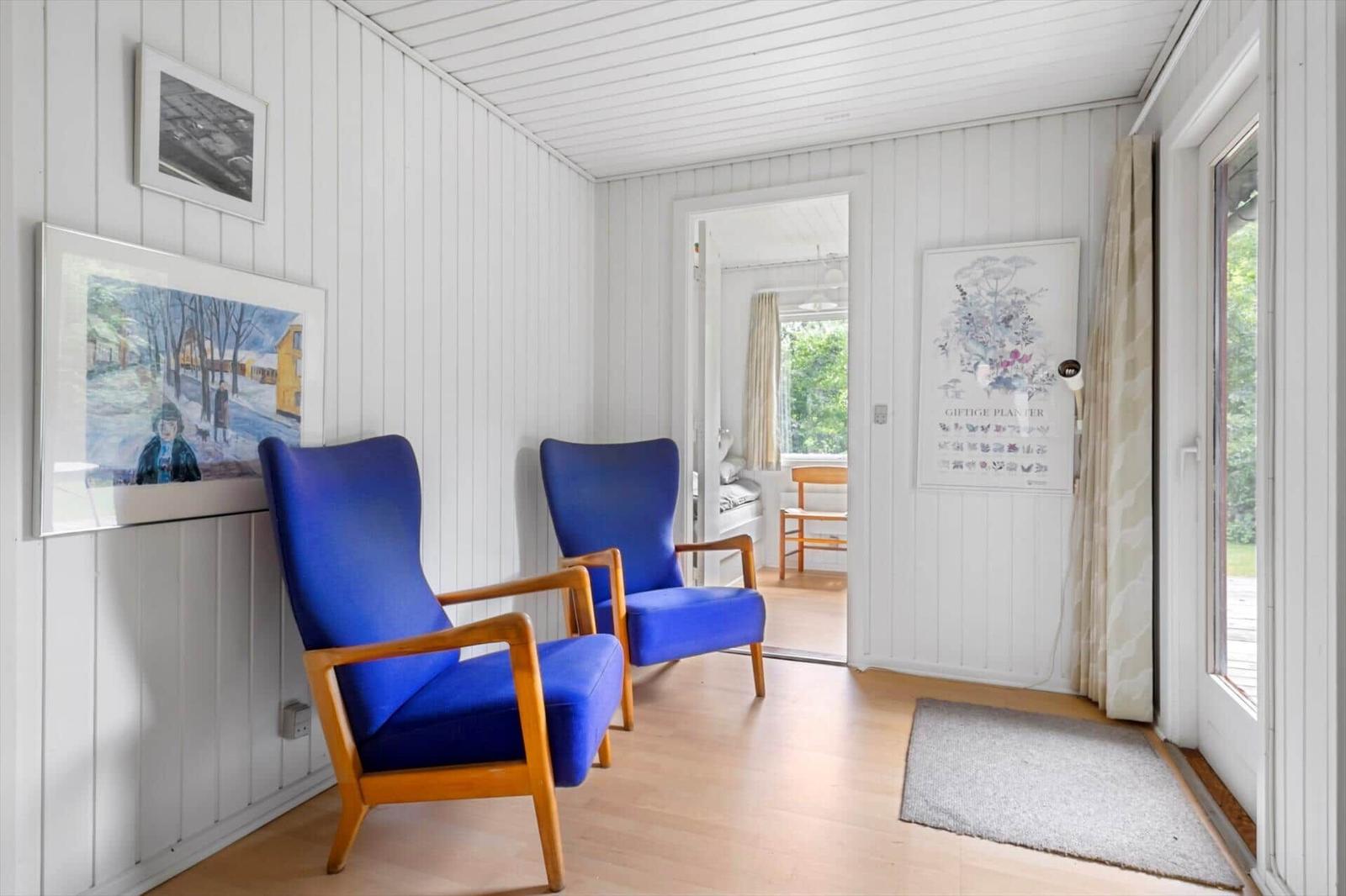 Zwei blaue Sessel stehen in einem Raum mit weißen Wänden und Holzboden. Durch Tür ist Schlafzimmer sichtbar.