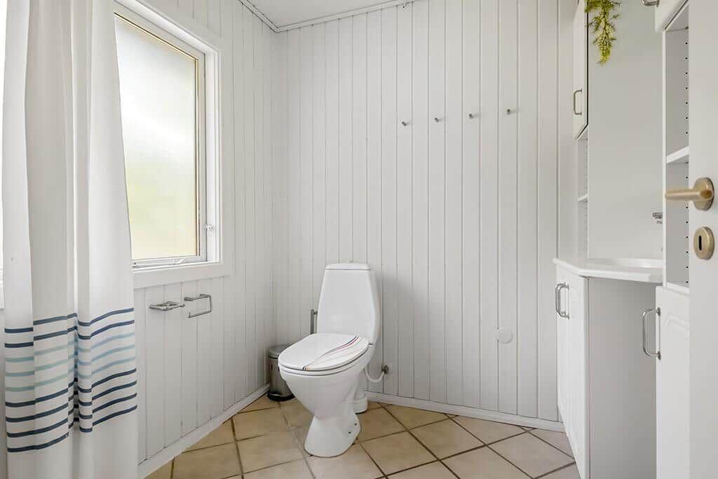 Badezimmer mit Toilette, Fenster und weißen Schränken.
