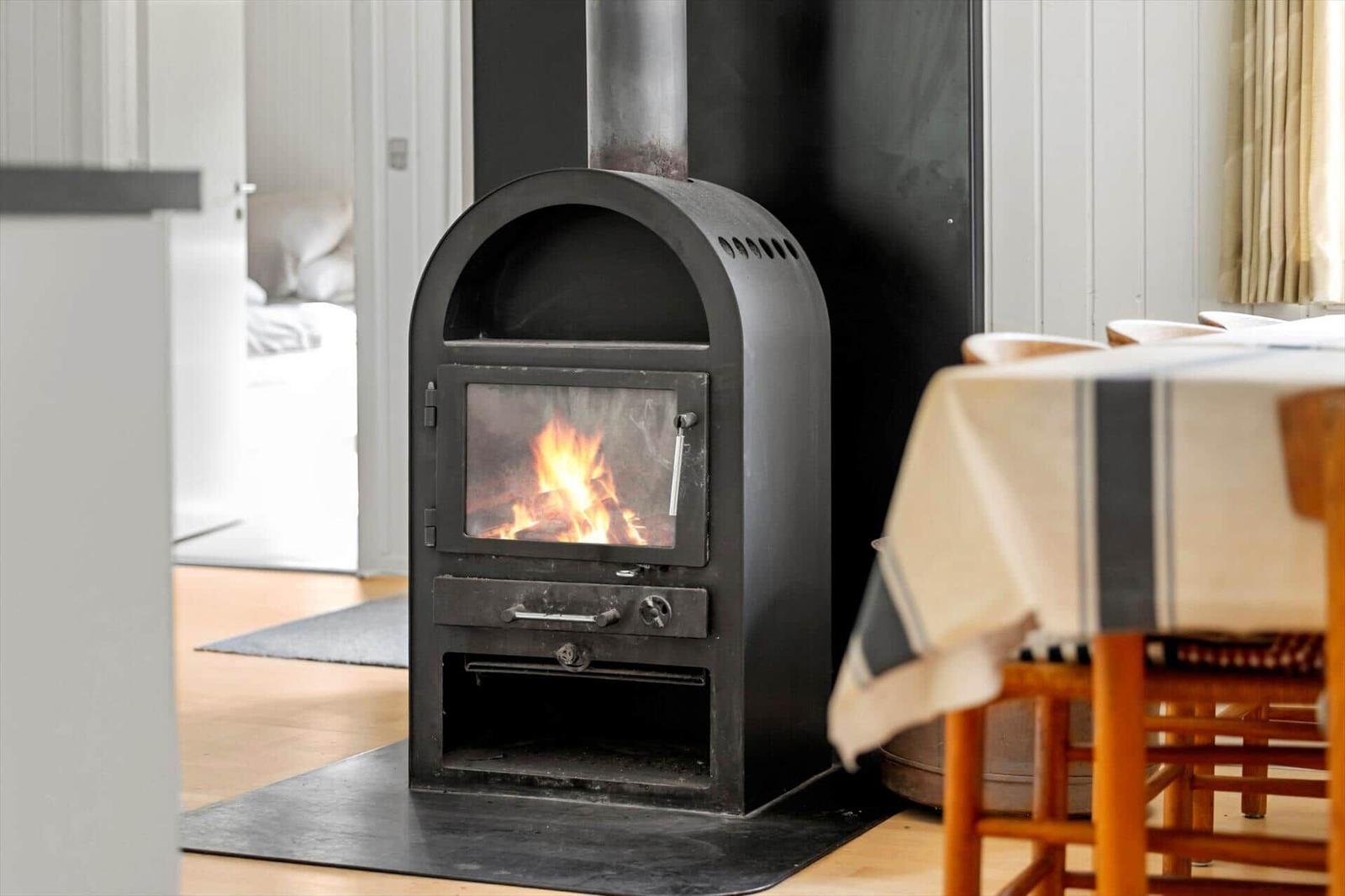 Ein schwarzer Kaminofen mit brennendem Feuer steht im Raum. Im Hintergrund ist ein Tisch mit Tischdecke zu sehen.