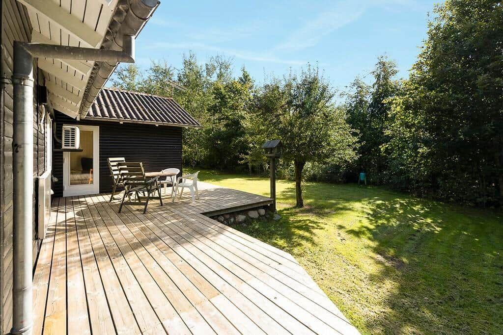 Terrasse mit Tisch und Stühlen neben einem Haus mit Garten und Bäumen.