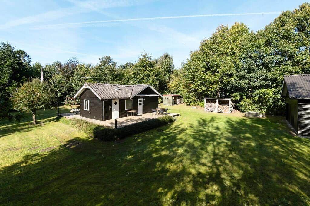 Holzhaus mit Terrasse, Grillplatz und Garten. Umgeben von Bäumen und Gras.