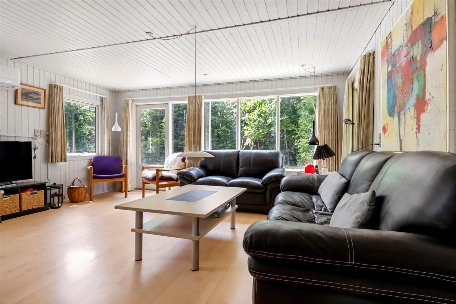 Wohnzimmer mit zwei schwarzen Sofas, Holzboden und großen Fenstern zur Außenseite.