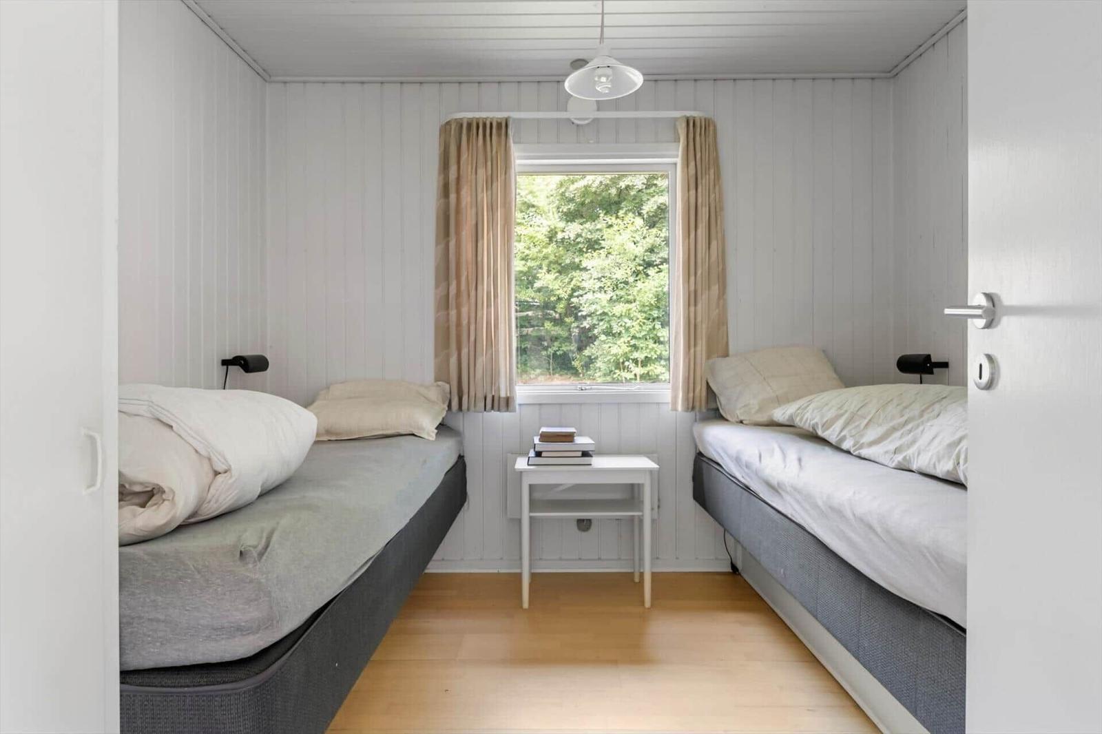 Zwei Einzelbetten mit Matratzen und Kissen stehen in einem Raum mit Holzboden und Fenster.