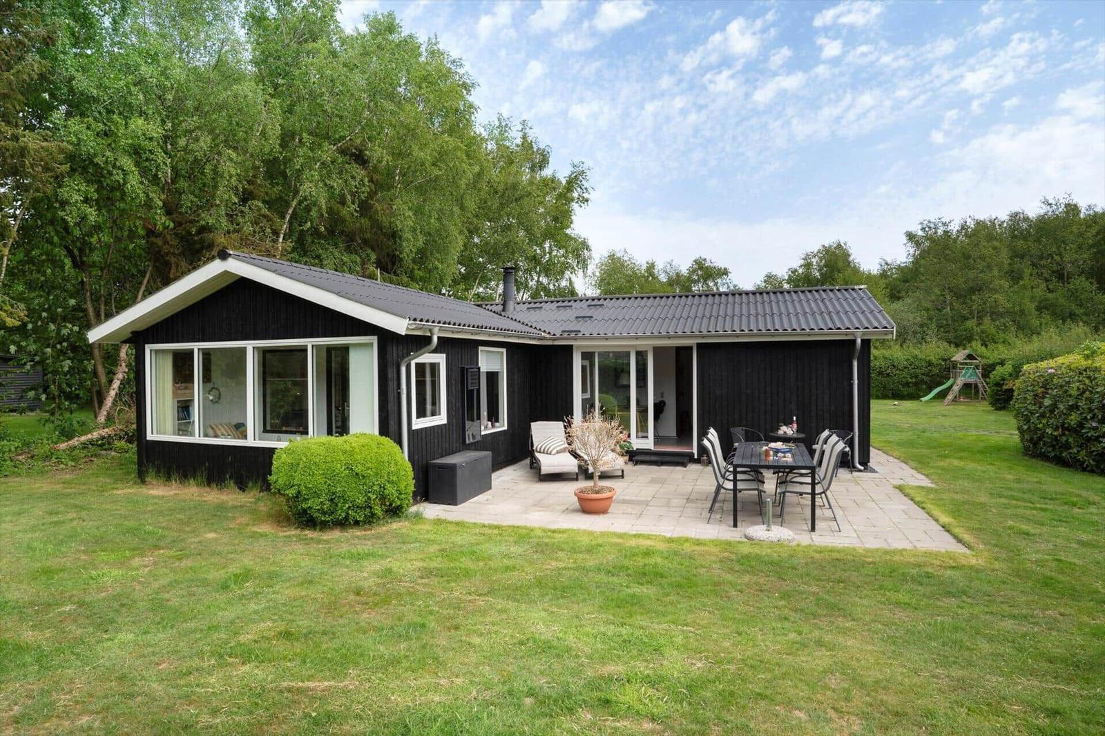 Schwarzes Haus mit Terrasse, Garten und Spielplatz. Modernes Design mit großzügigen Fenstern.
