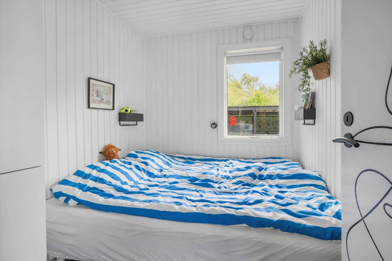 Schlafzimmer mit Bett, blau-weißem Bettbezug, Fenster und Wanddekoration.
