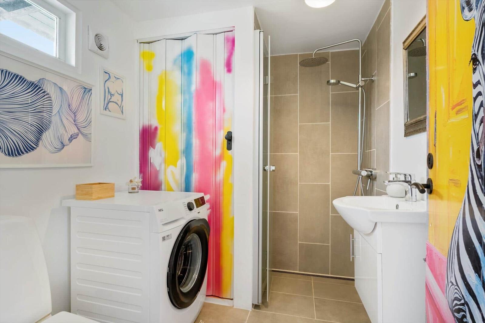 Badezimmer mit Dusche, Waschmaschine und bunt bemalter Tür.