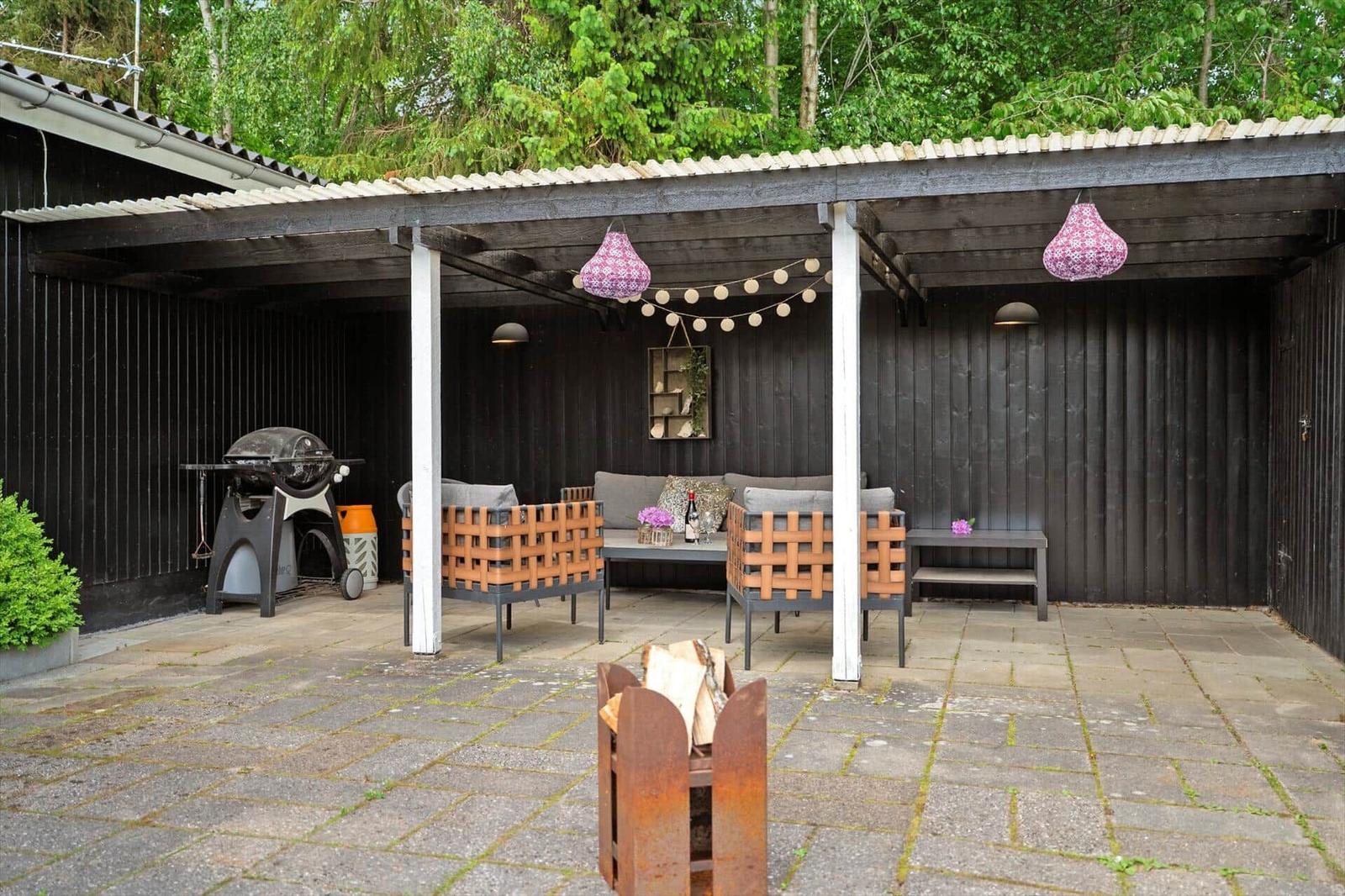 Außenbereich mit Sitzgruppe, Grill und Feuerkorb unter Dach.