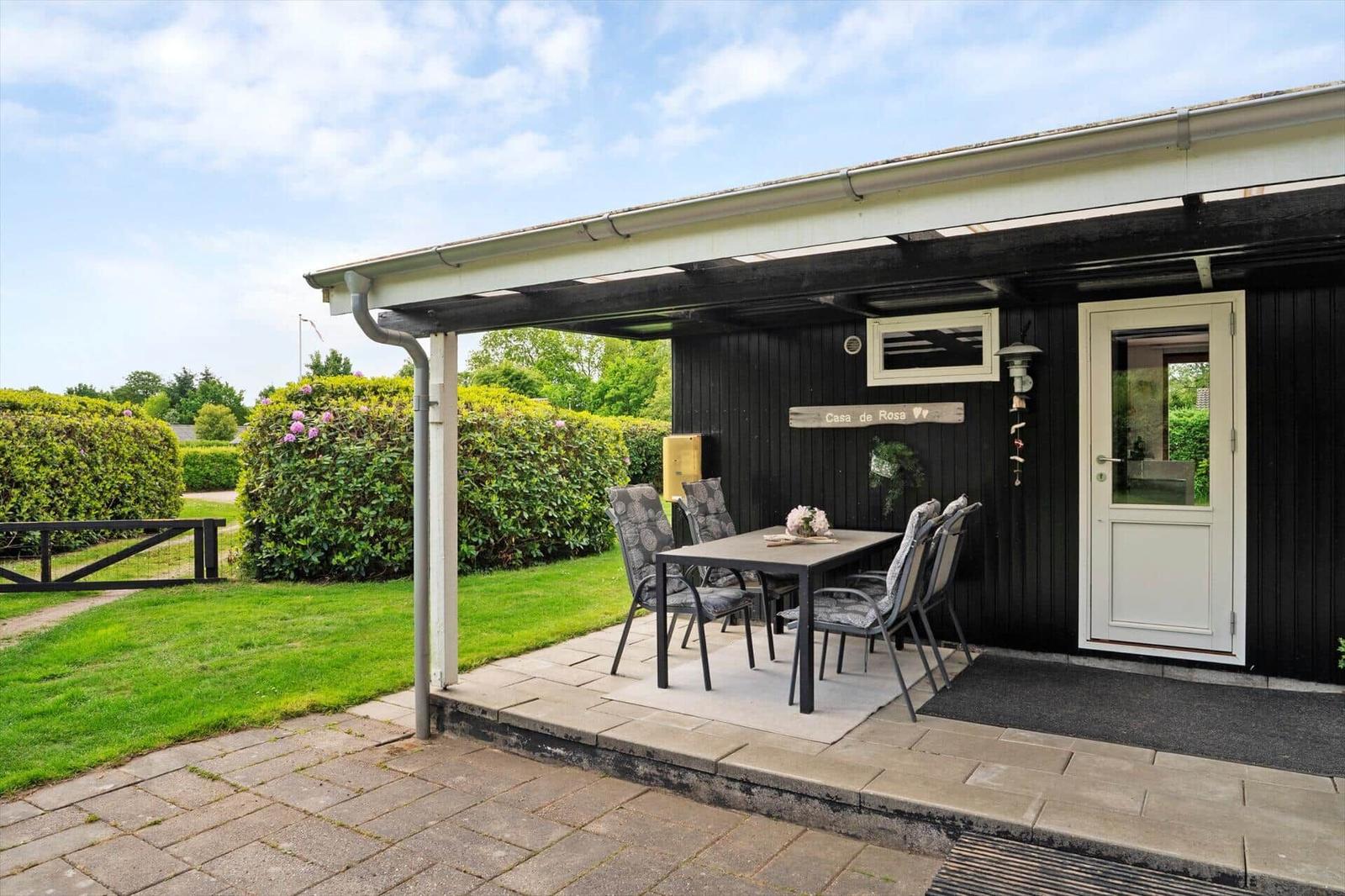 Terrasse mit Tisch und Stühlen vor einem schwarz verkleideten Haus mit weißer Tür.