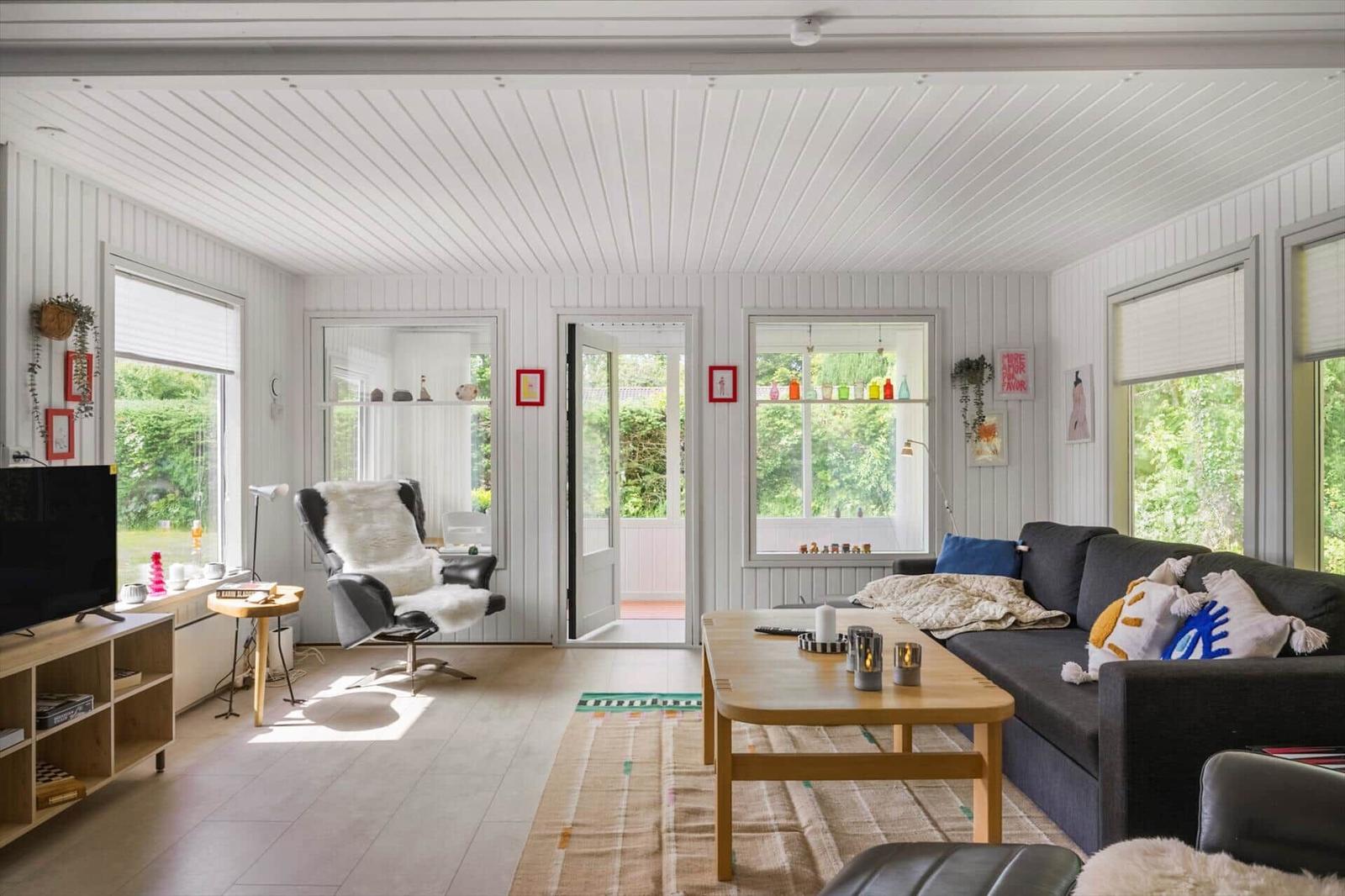 Wohnzimmer mit Sofa, Couchtisch und Sessel. Fenster und Tür zur Außenterrasse.