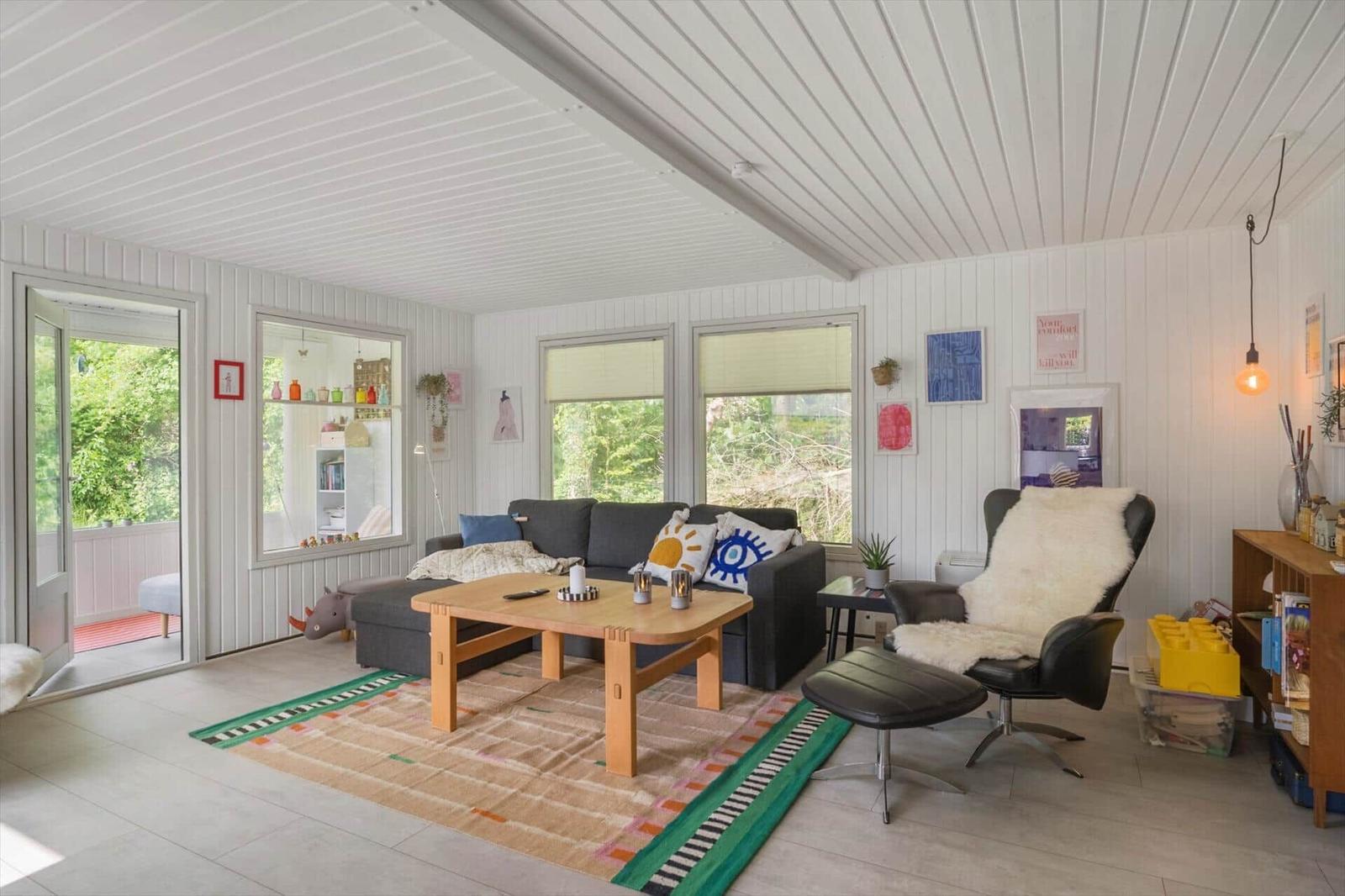 Wohnzimmer mit Sofa, Sessel und Holztisch. Fenster und Tür zeigen Garten.