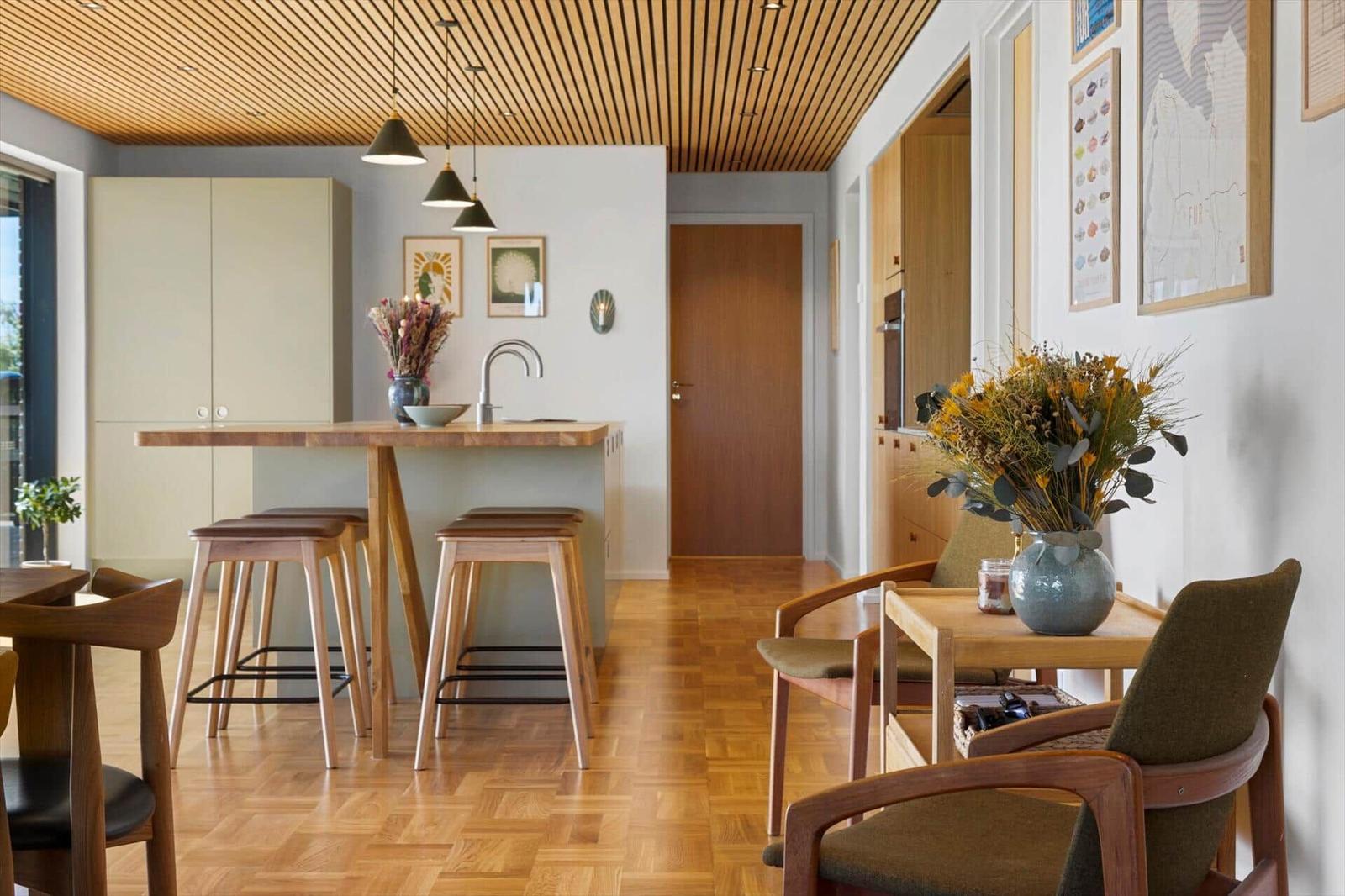 Kitchen with wooden ceiling, bar stools, and dining area with chairs.