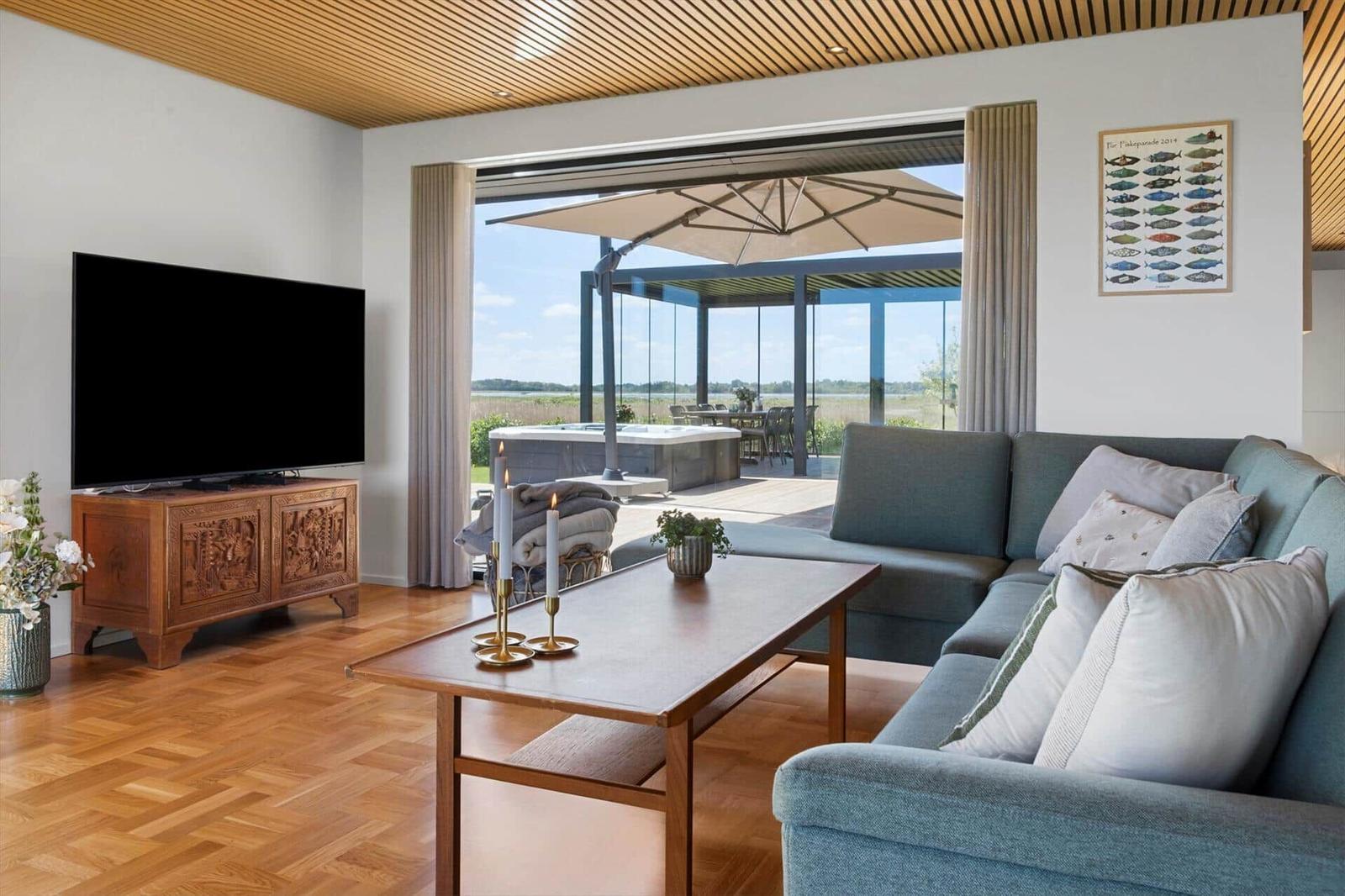 Living room with sofa, coffee table, and TV. Terrace with umbrella and hot tub.