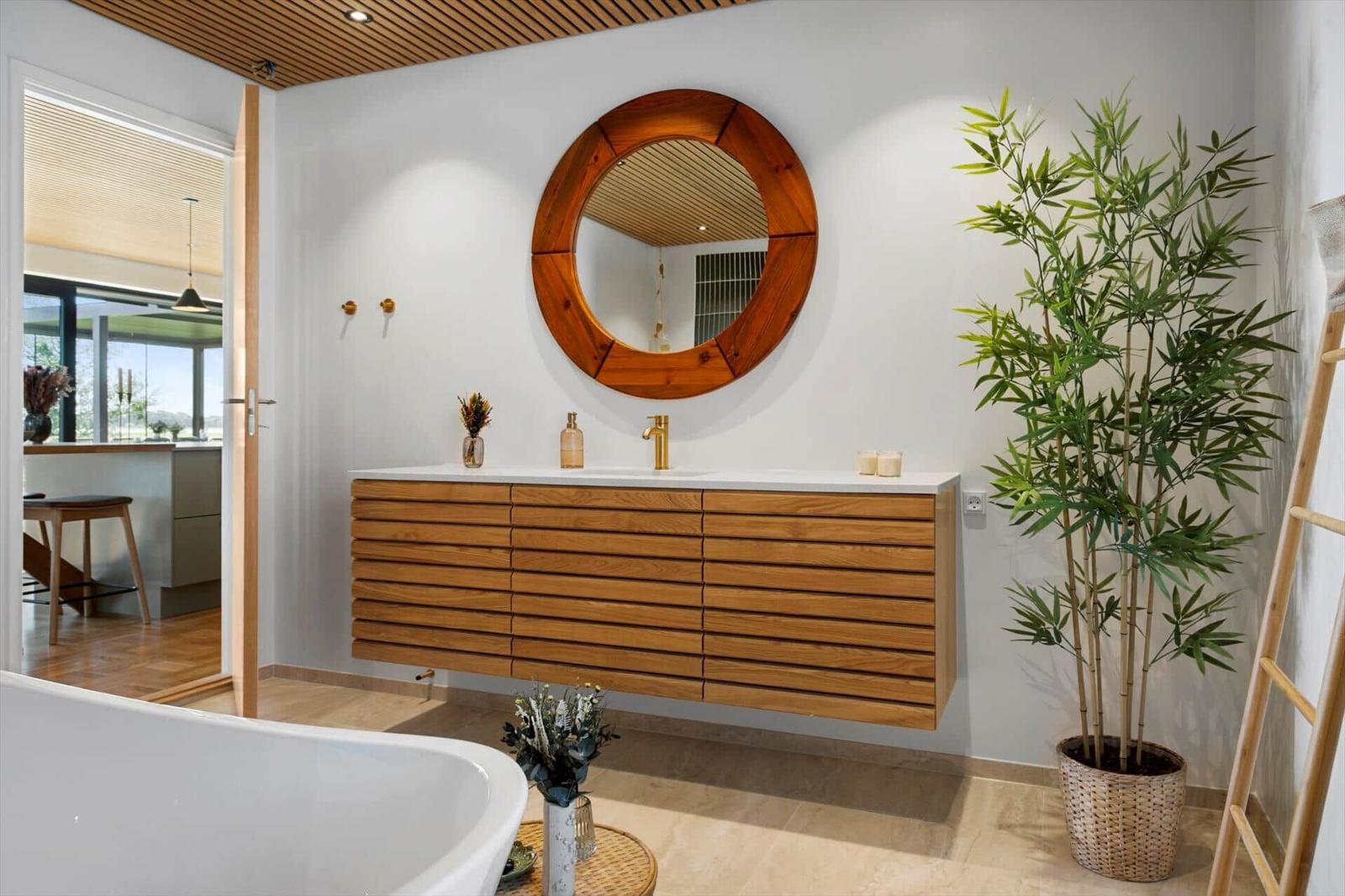 Bathroom with wooden vanity, round mirror, and plant.