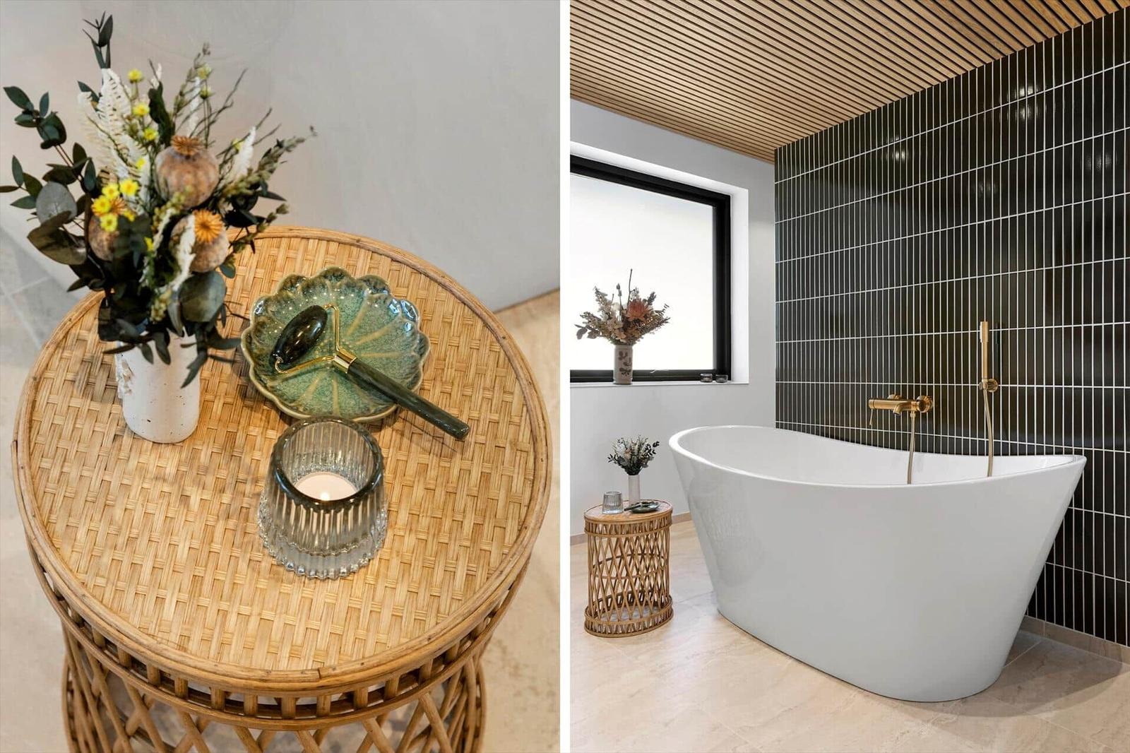 Rattan table with flowers and candle beside freestanding bathtub.