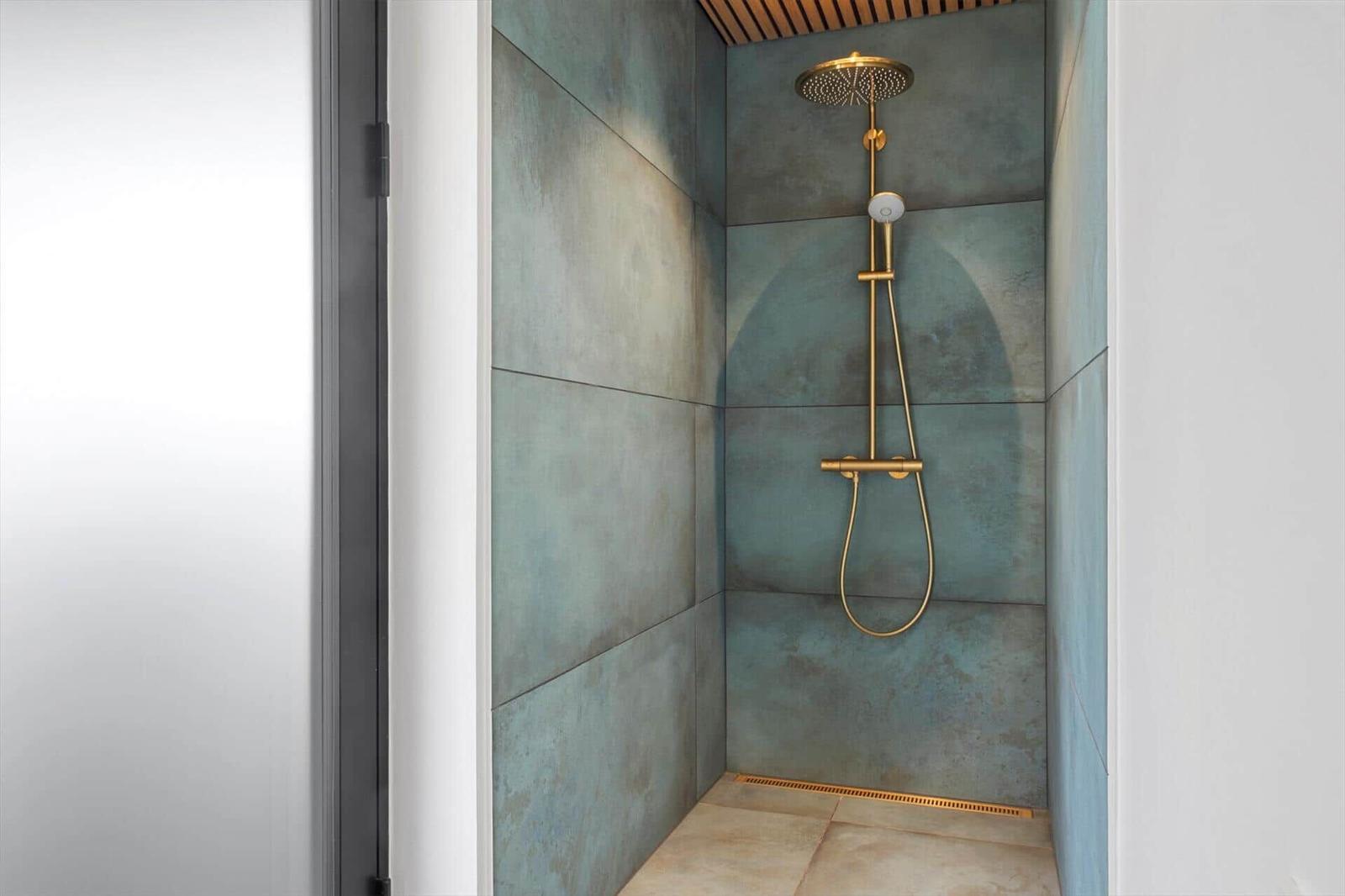 Shower with gold fixtures and blue-gray wall tiles.