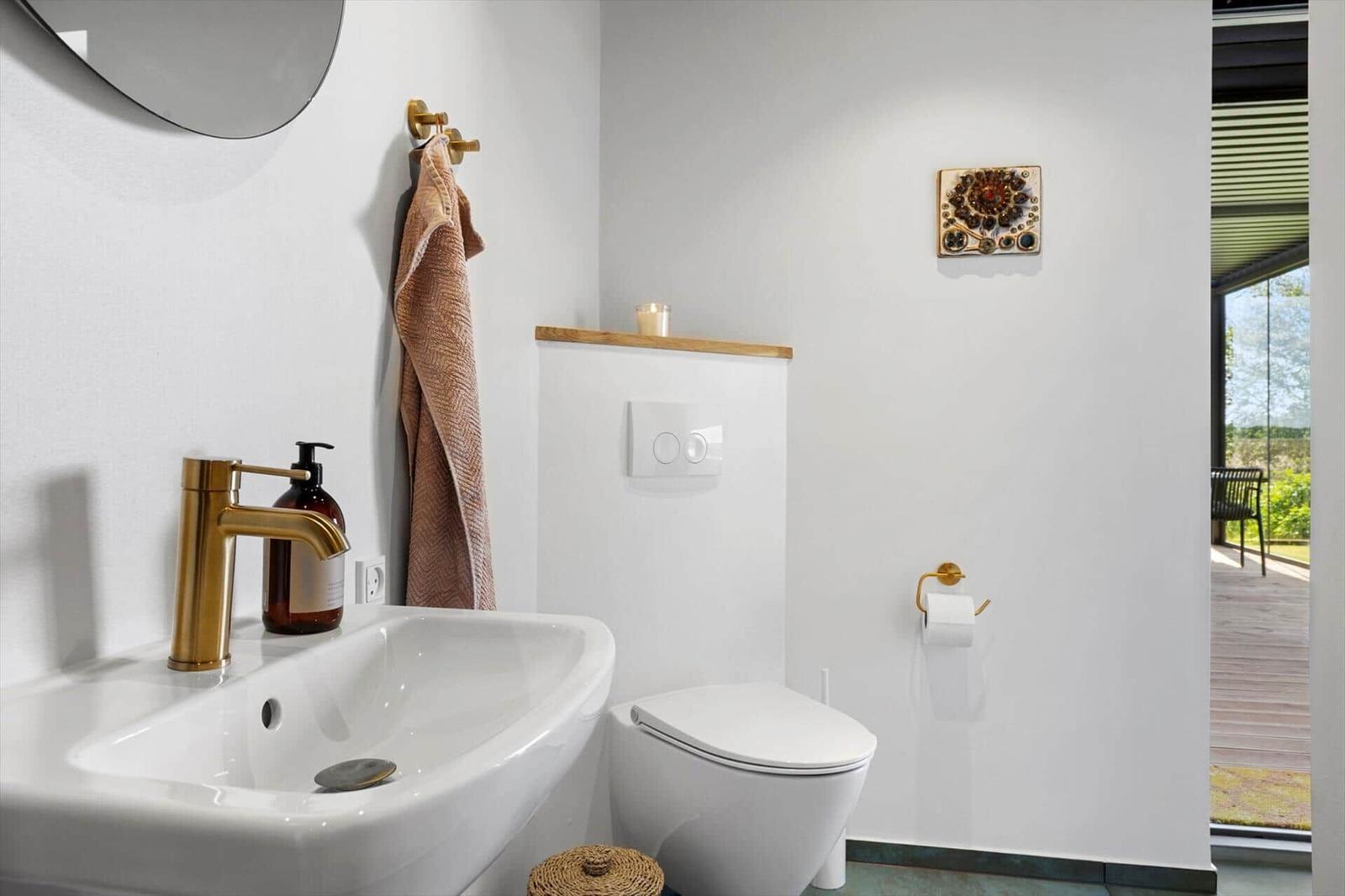 Bathroom with sink, toilet, and wooden shelf. View of terrace.