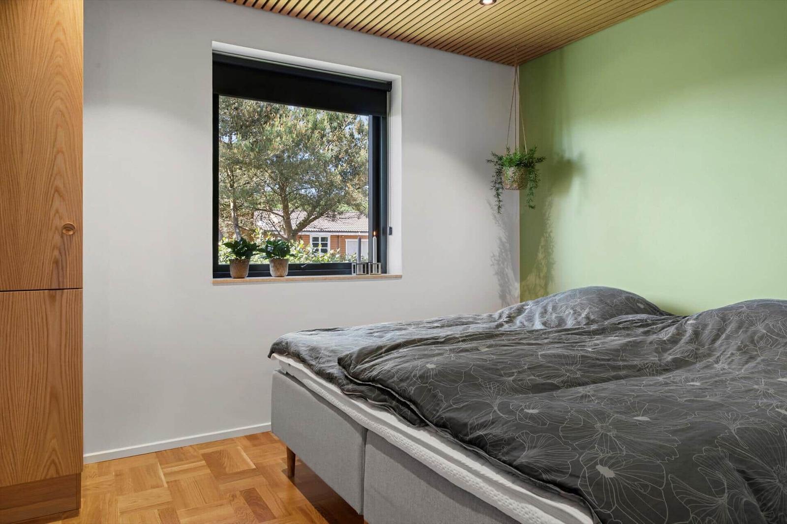 Bedroom with bed, wooden floor, and window with view of trees.
