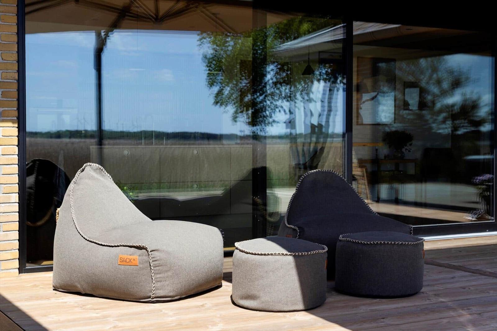 Outdoor area with two bean bags and two ottomans on wooden terrace near large window.