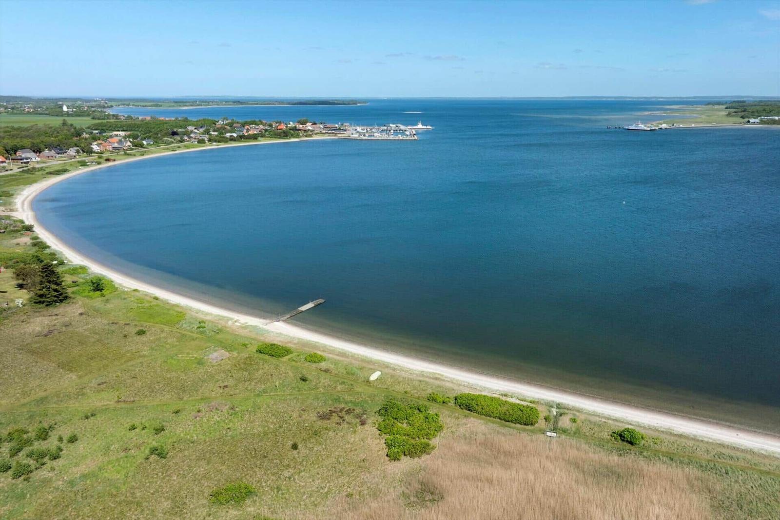 Aerial view of a beach with sea, marina, and green landscape.