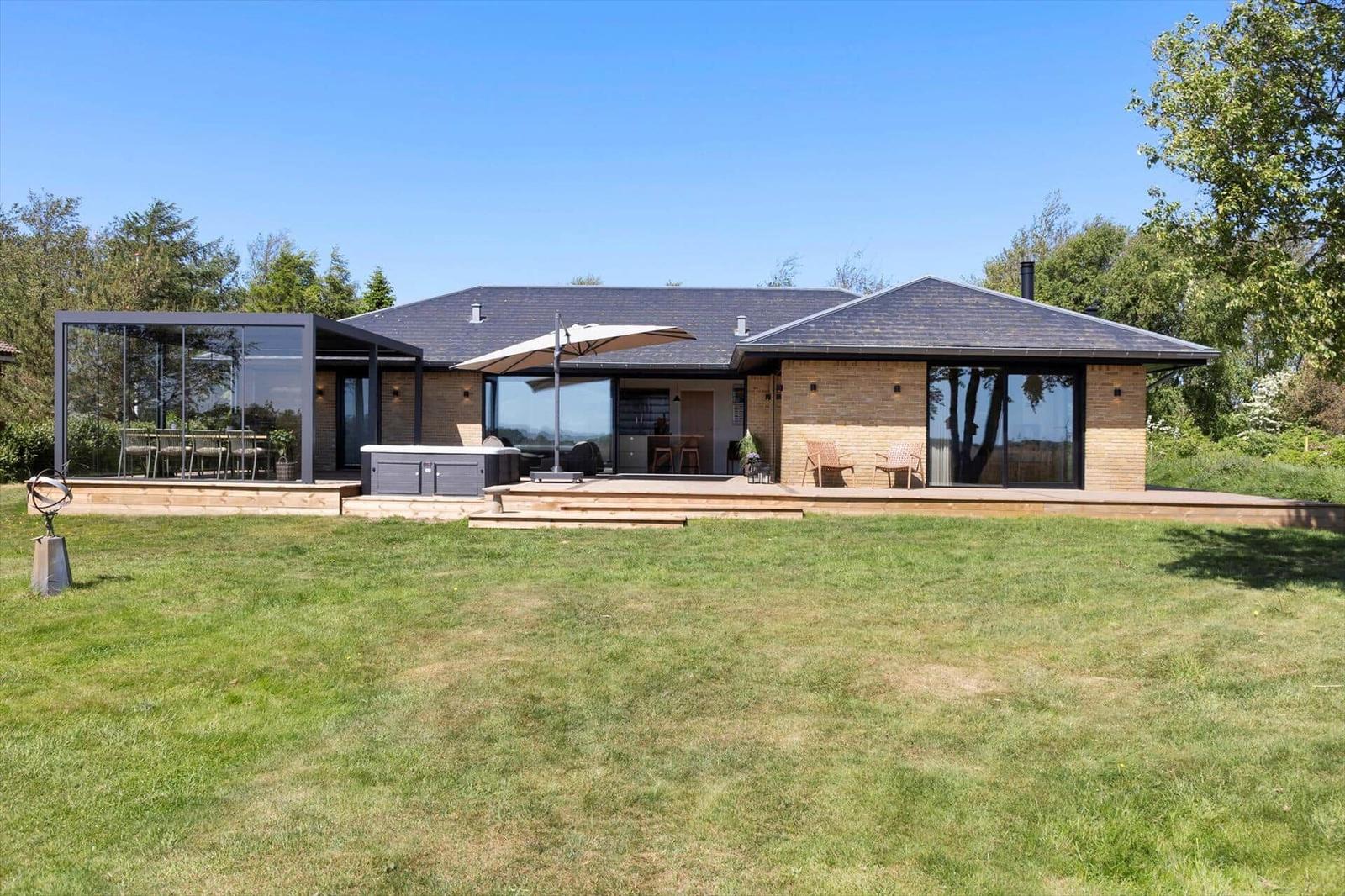 Modern villa with terrace, hot tub, and garden. Glass veranda and seating areas.