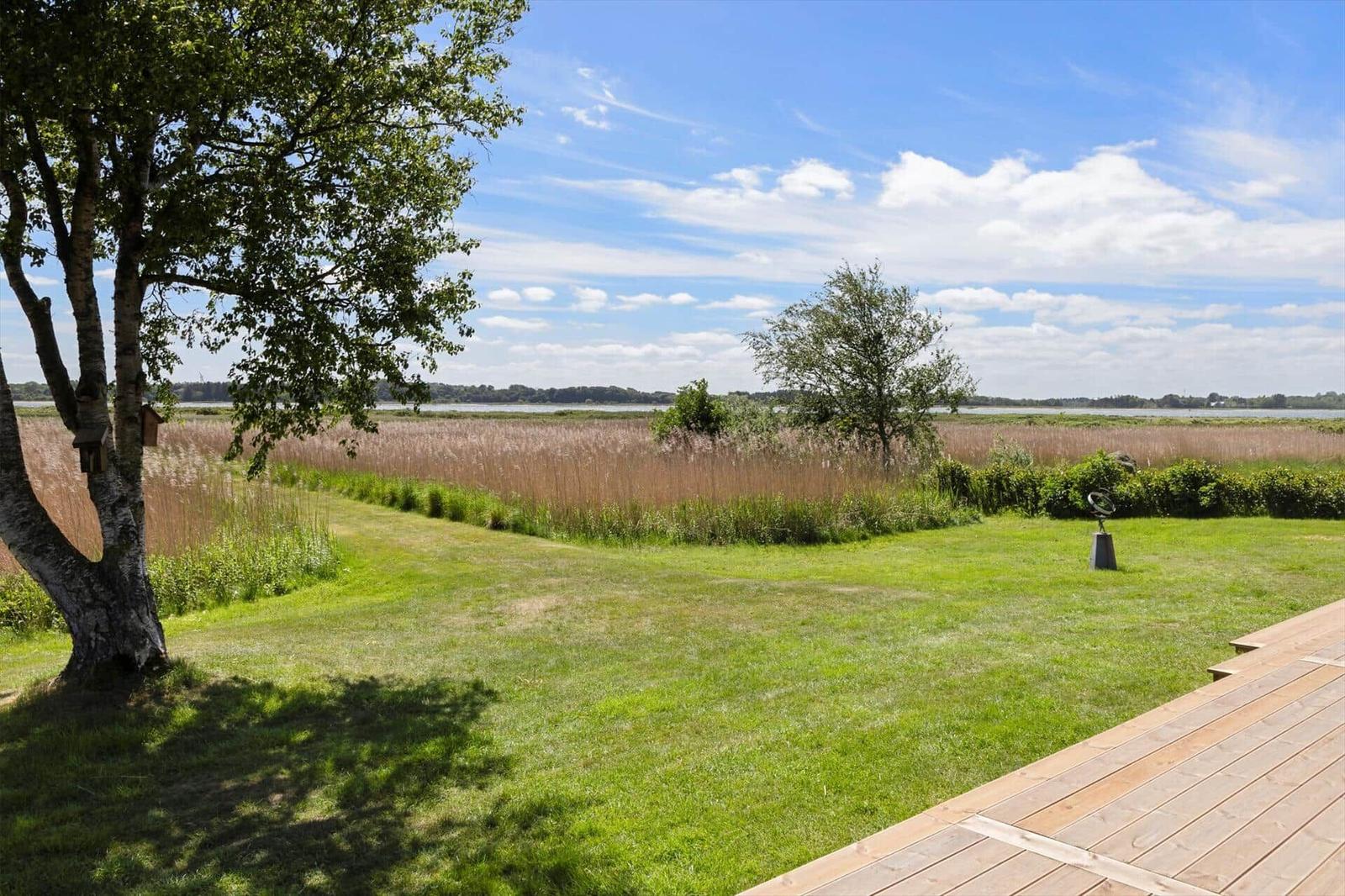 Green lawn with wooden terrace, view of a lake and trees.