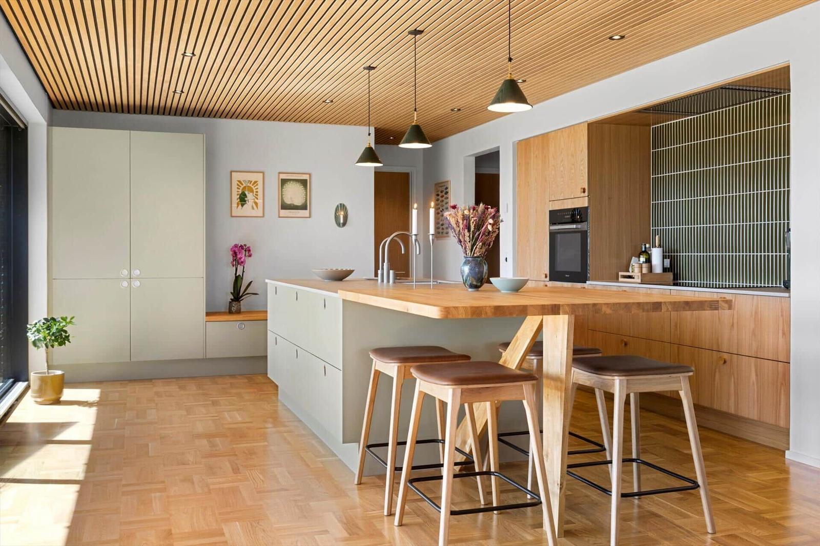 Kitchen with wooden ceiling, island, and bar stools. Wooden floor and modern furnishings.