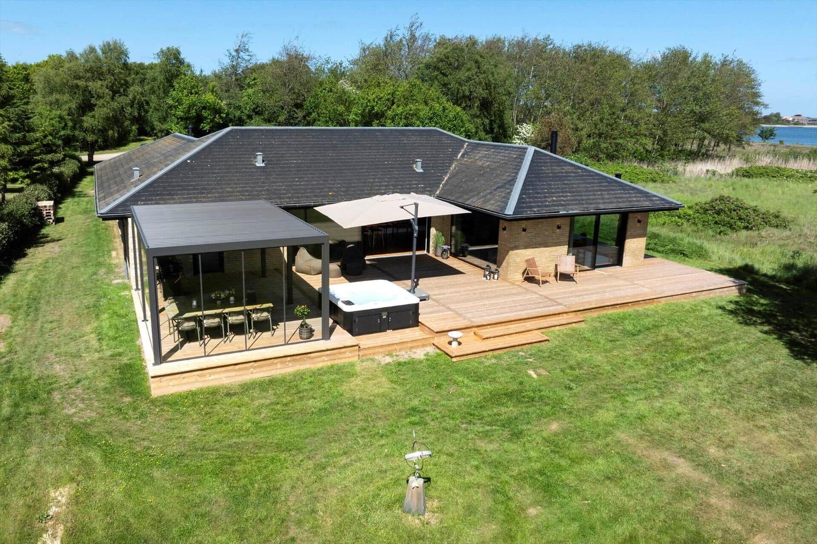 Modern villa with terrace, hot tub, and garden. View of water and forest.