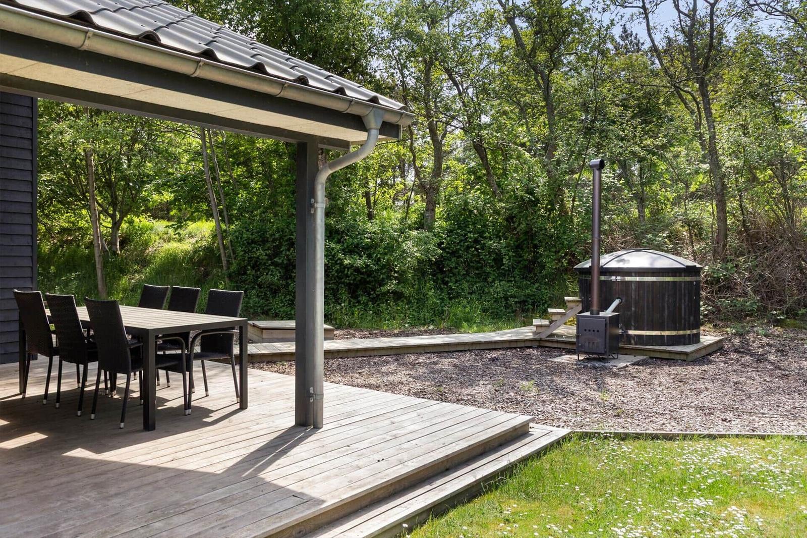 Terrasse mit Tisch und Stühlen, Whirlpool und Wald im Hintergrund.