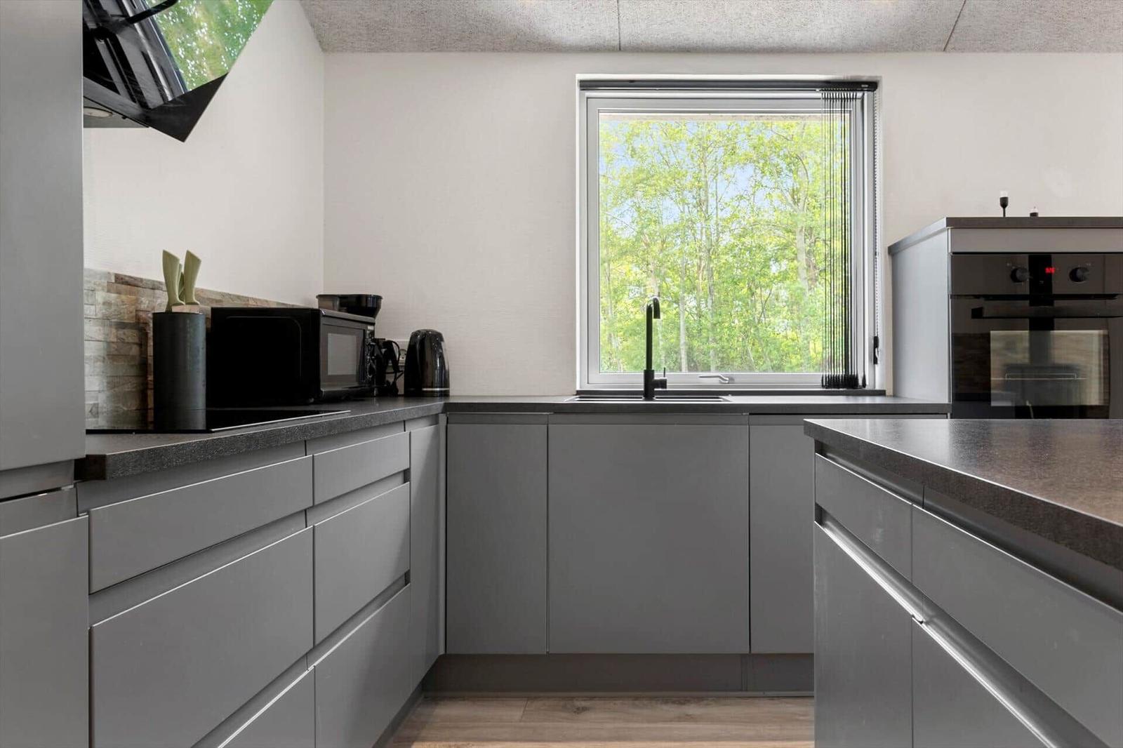 Küche mit grauen Schränken, Fenster mit Blick auf Bäume und schwarze Geräte.