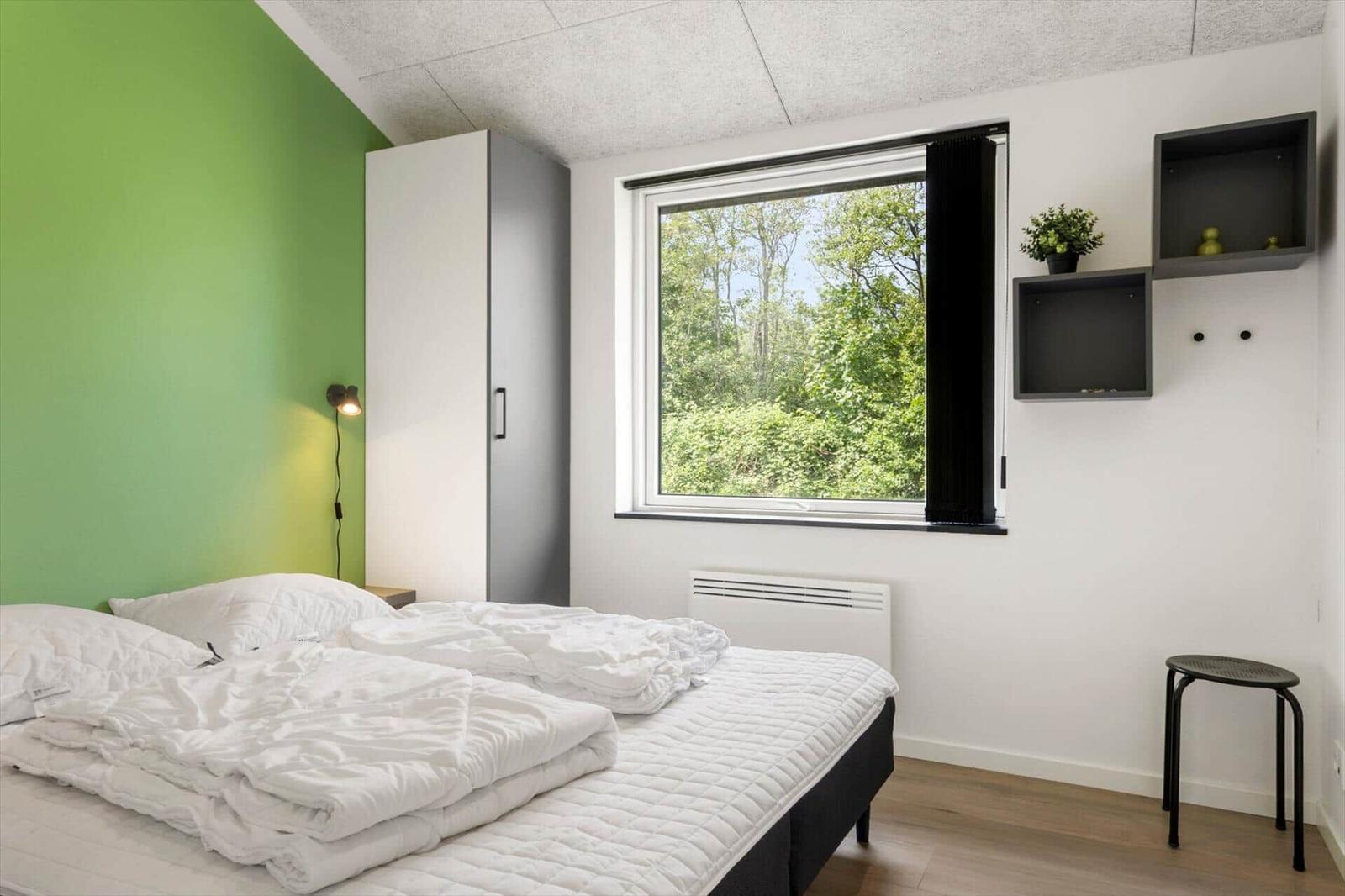 Schlafzimmer mit grüner Wand, Bett, Fenster und Wandregalen.