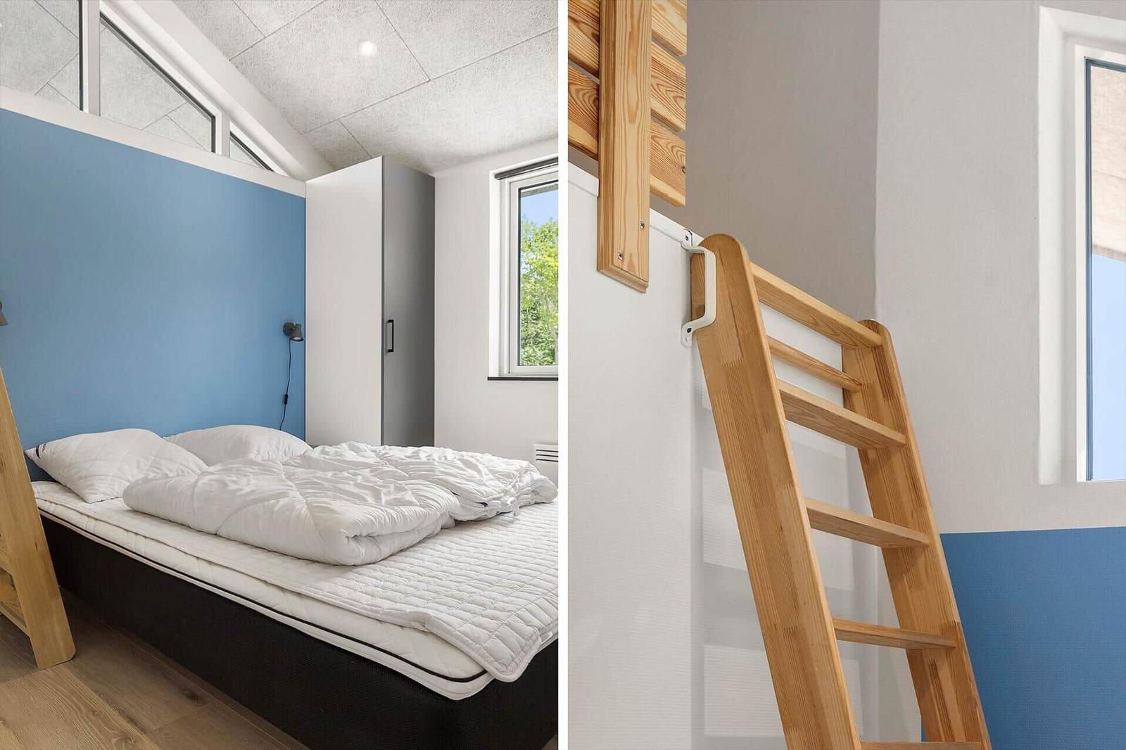 Schlafzimmer mit Bett und Holztreppe zur oberen Etage. Wand in Blau und Weiß.