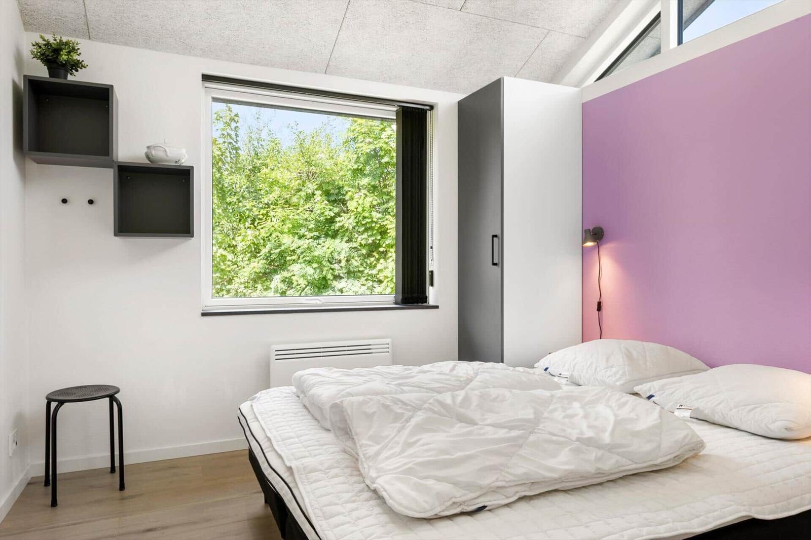 Schlafzimmer mit Bett, Fenster und lila Wand