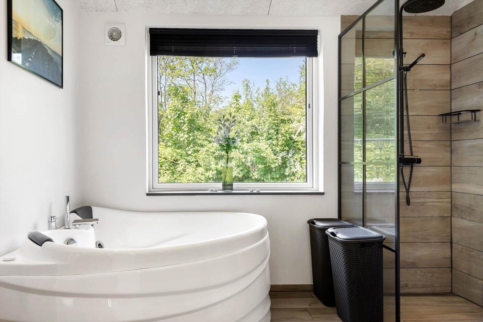 Bad mit Whirlpool, Dusche und Fensterblick auf grüne Bäume.