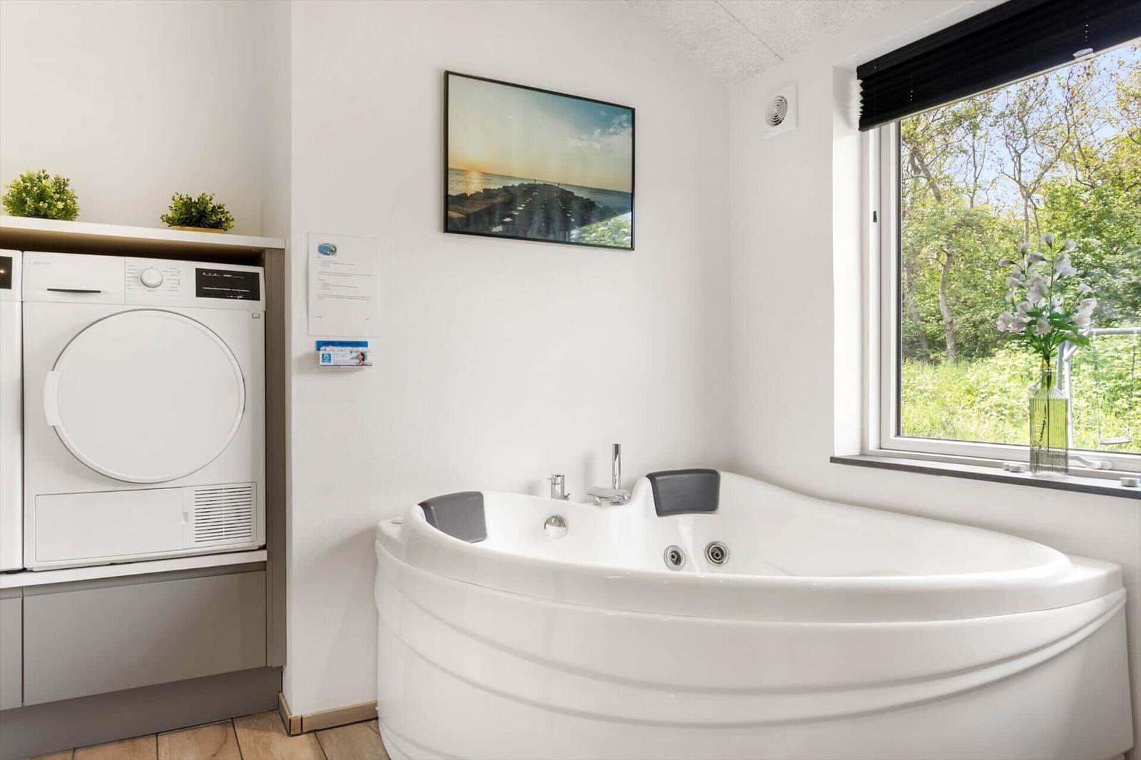 Bad mit Whirlpool, Fenster mit Blick auf Grün, Waschmaschine und Wandbild.