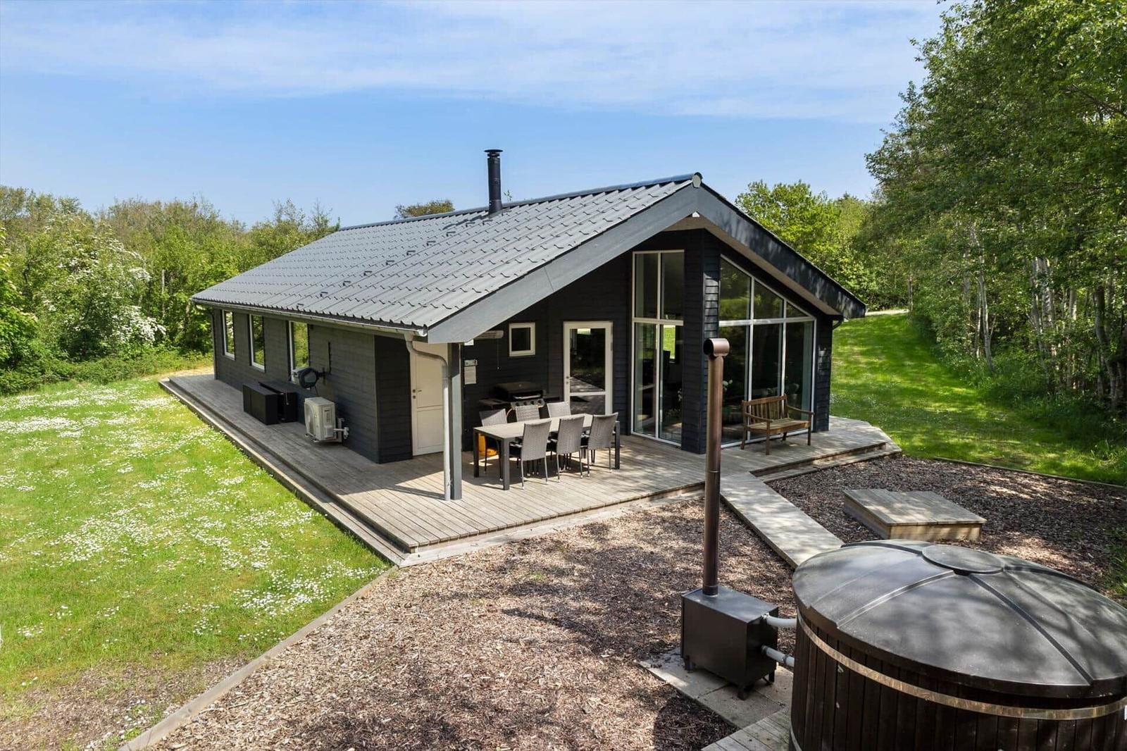 Moderne Holzhütte mit Terrasse, Grill und Whirlpool im Grünen.