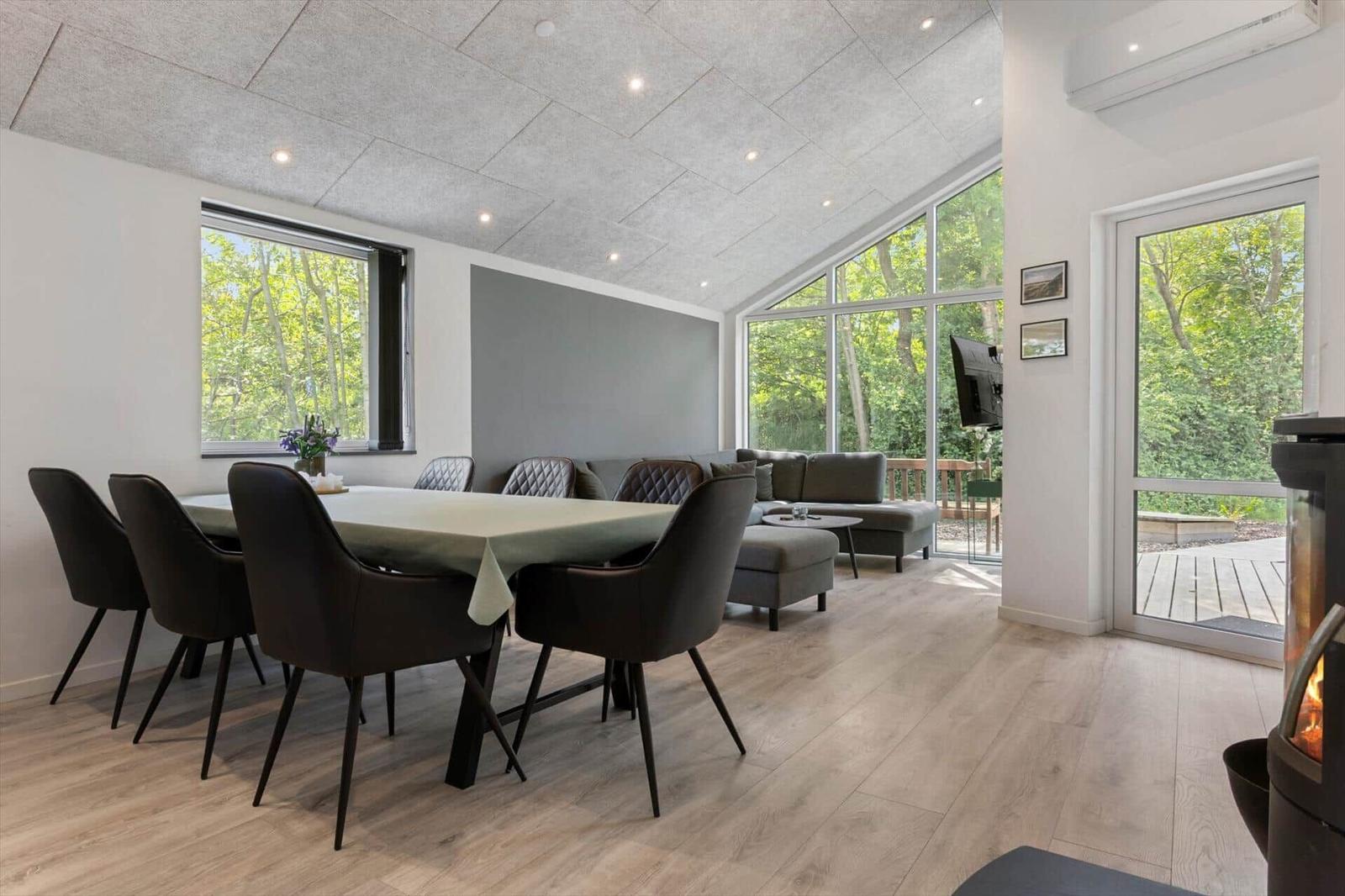 Esszimmer mit Tisch, Stühlen und Sofa. Große Fenster und Terrasse. Kamin im Vordergrund.