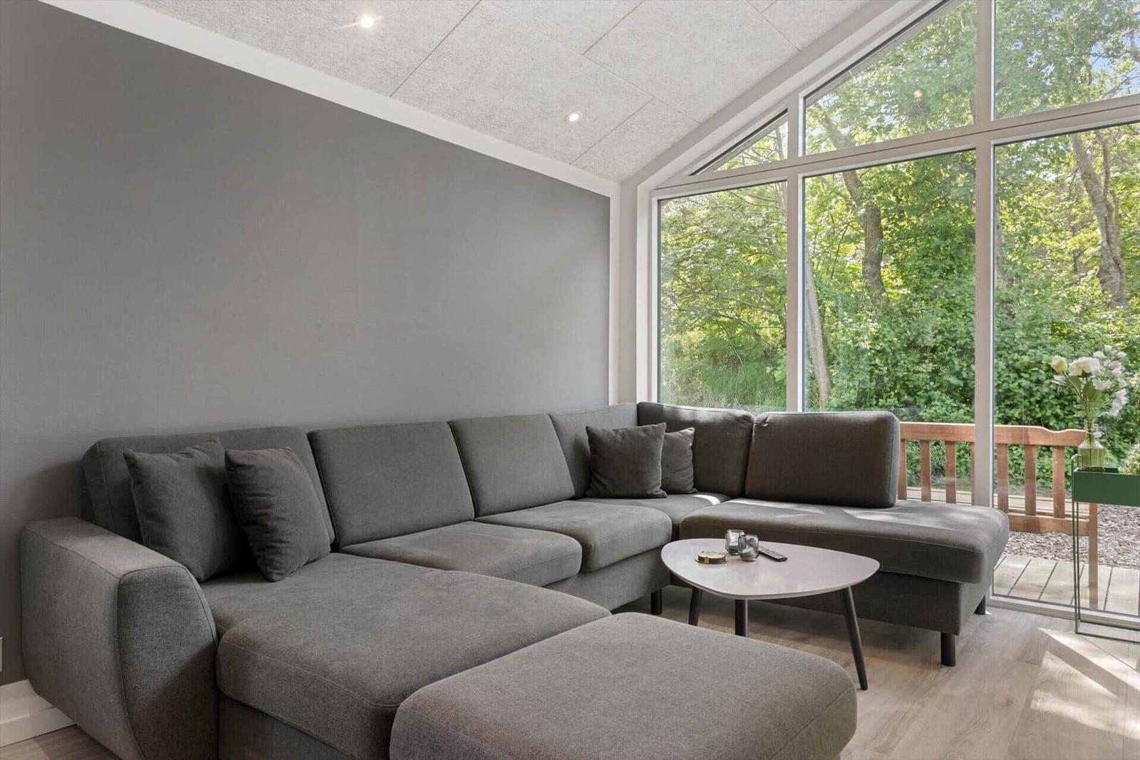 Großer Wohnbereich mit grauem Sofa und großem Fenster zum Garten.