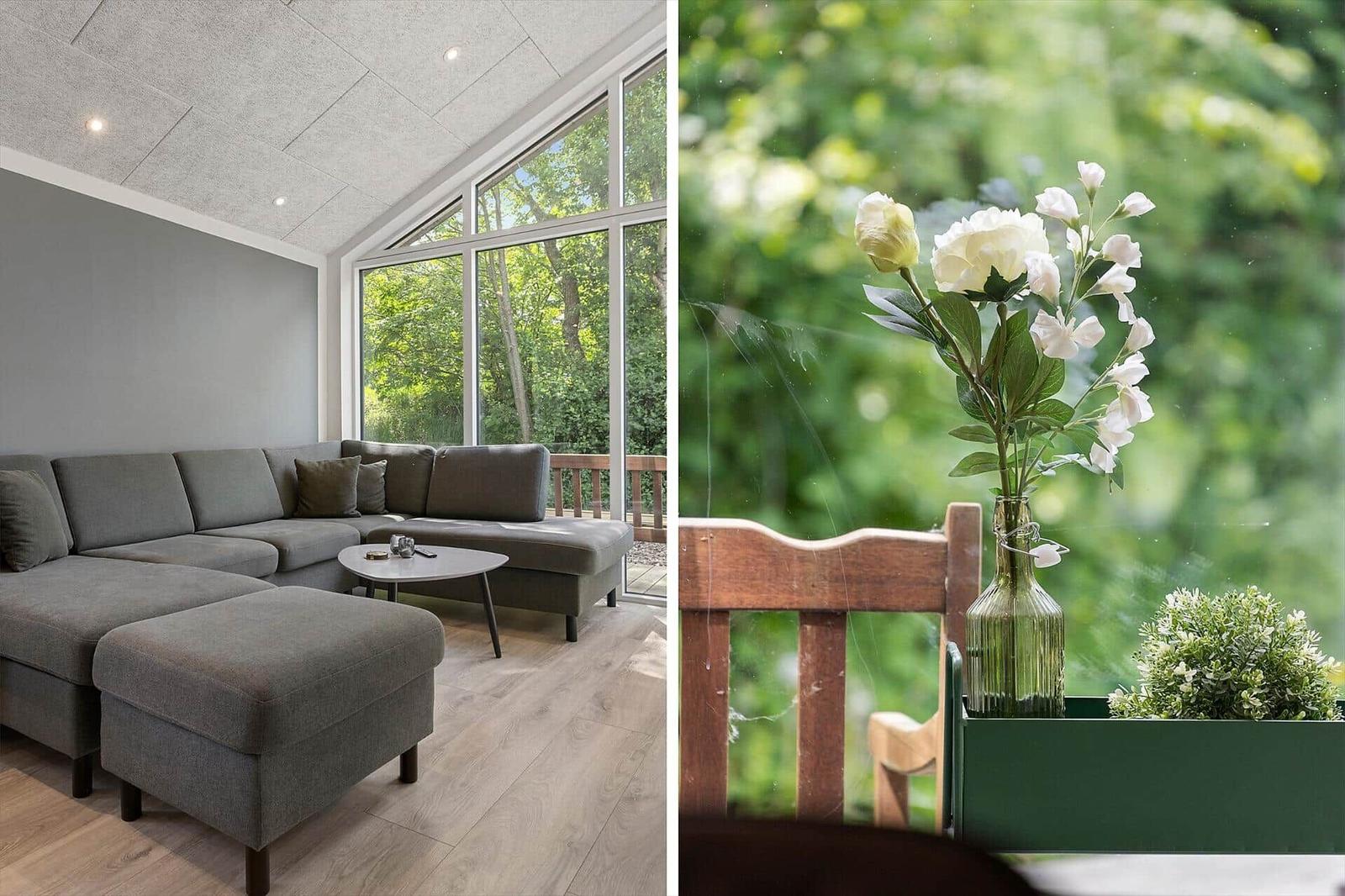 Wohnzimmer mit grauem Sofa und großem Fenster. Blumen in Glasflasche auf Balkon.