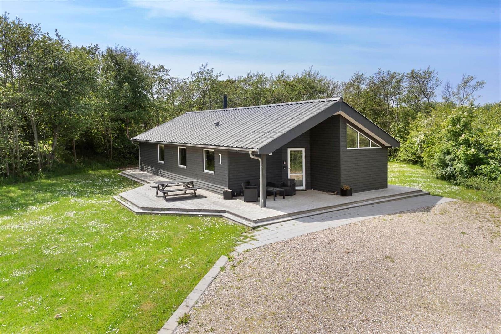 Ein modernes Haus mit Terrasse, Garten und Grillplatz. Umgeben von Bäumen und Gras.