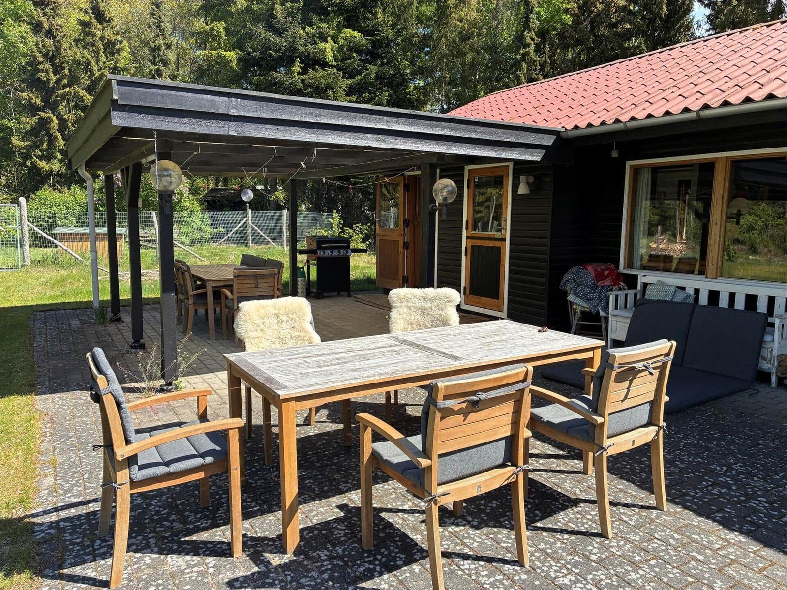 Terrasse mit Tisch, Stühlen und Grill unter Pavillon. Hintergrund: Haus mit rotem Dach.