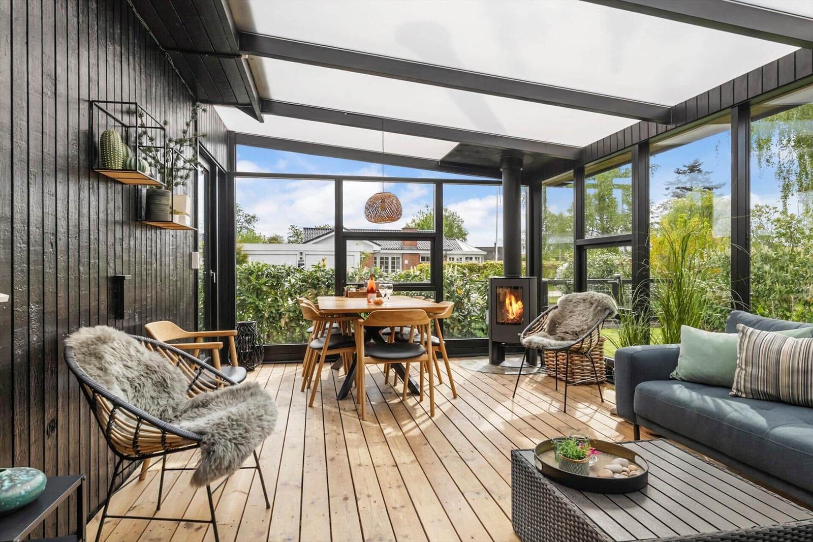 Terrasse mit Sitzgruppe, Esstisch und Kaminofen. Holzdielenboden und großflächige Glaswände.