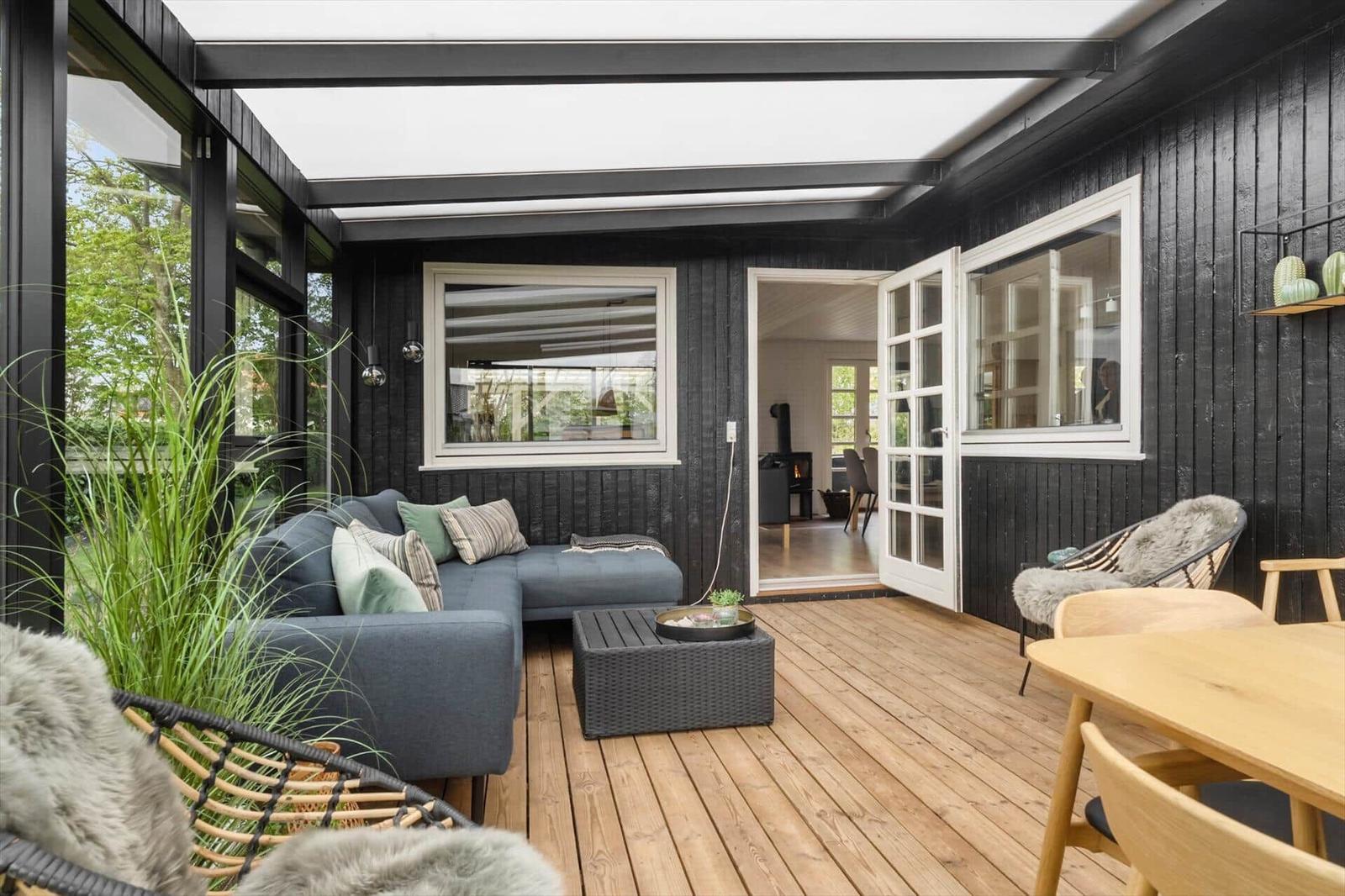 Terrasse mit Sofa, Tisch und Stühlen. Holzdielen und schwarze Wände.