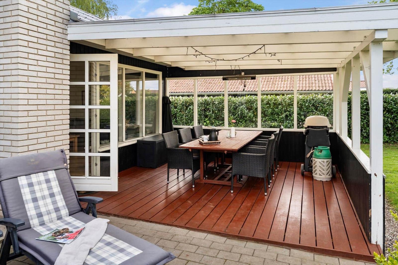 Terrasse mit Tisch, Stühlen und Sonnenschutz. Holzdecke, Gartenmöbel und Grillplatz.