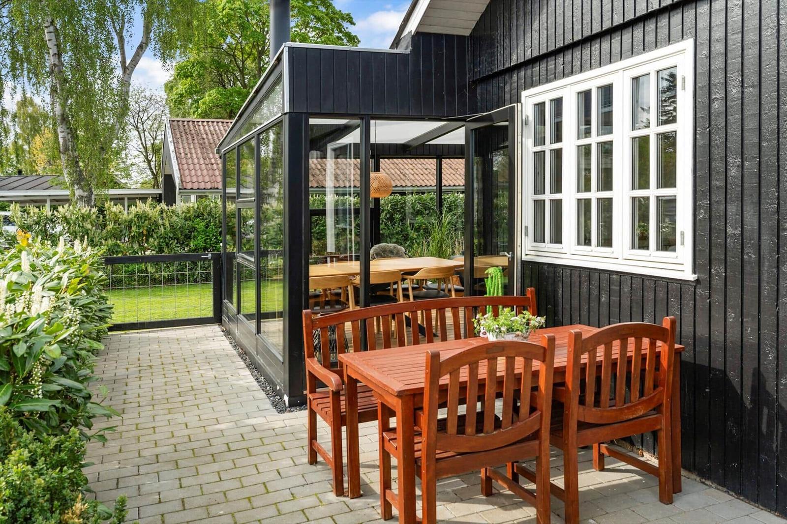 Hinterhof mit Holztisch, Stühlen und Glasveranda an schwarzem Holzhaus.