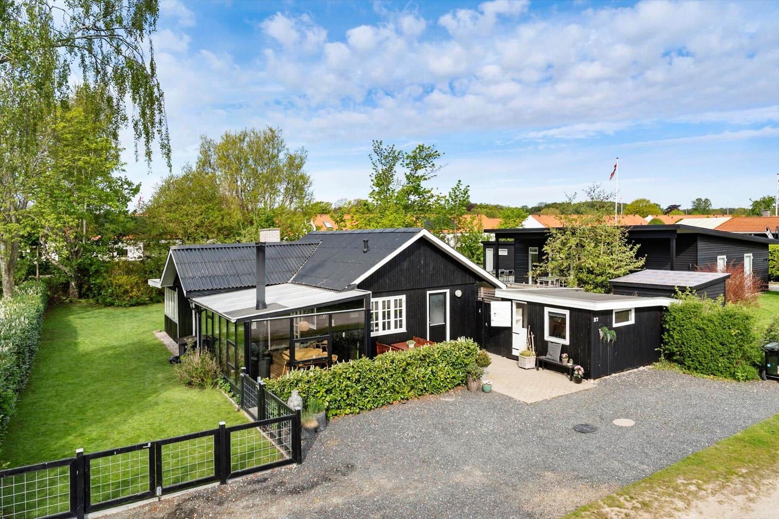 Schwarze Holzhütte mit Terrasse, Garten und Grillplatz. Hinterhof mit Rasenfläche und Zäunen.
